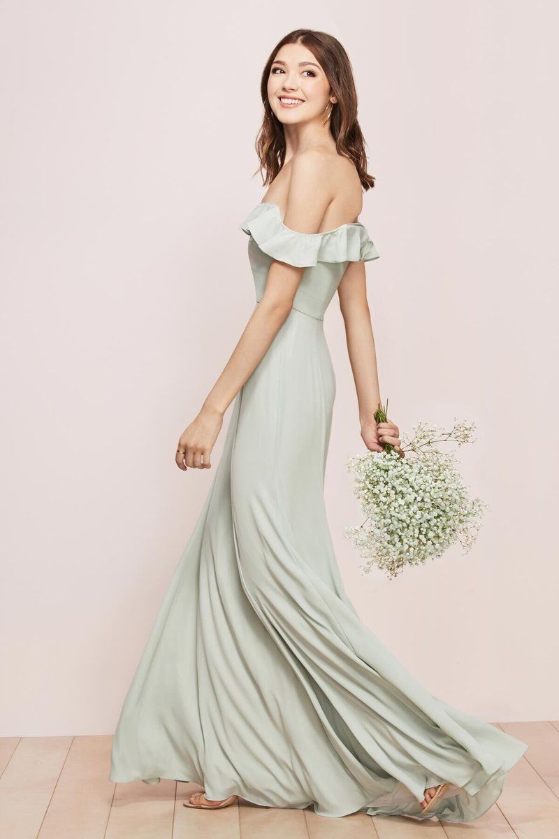 Woman in a pale green off-shoulder gown holding a bouquet of flowers against a soft pink backdrop