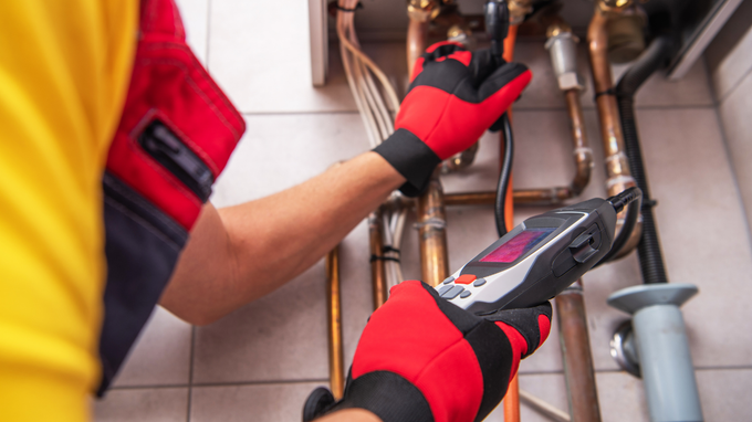 Person wearing red gloves adjusting plumbing pipes with a wrench under a sink