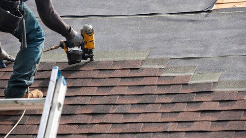 Worker using a nail gun installing shingles on a roof