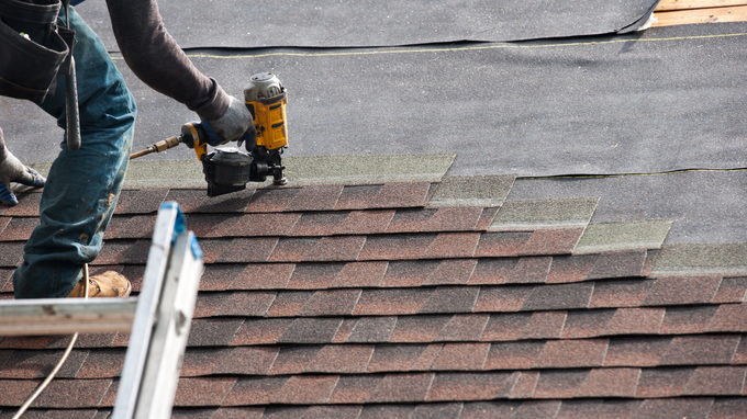 Worker using a nail gun installing shingles on a roof