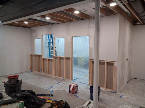 Partially renovated room with exposed studs, drywall, plastic covering, and a blue ladder near a doorway
