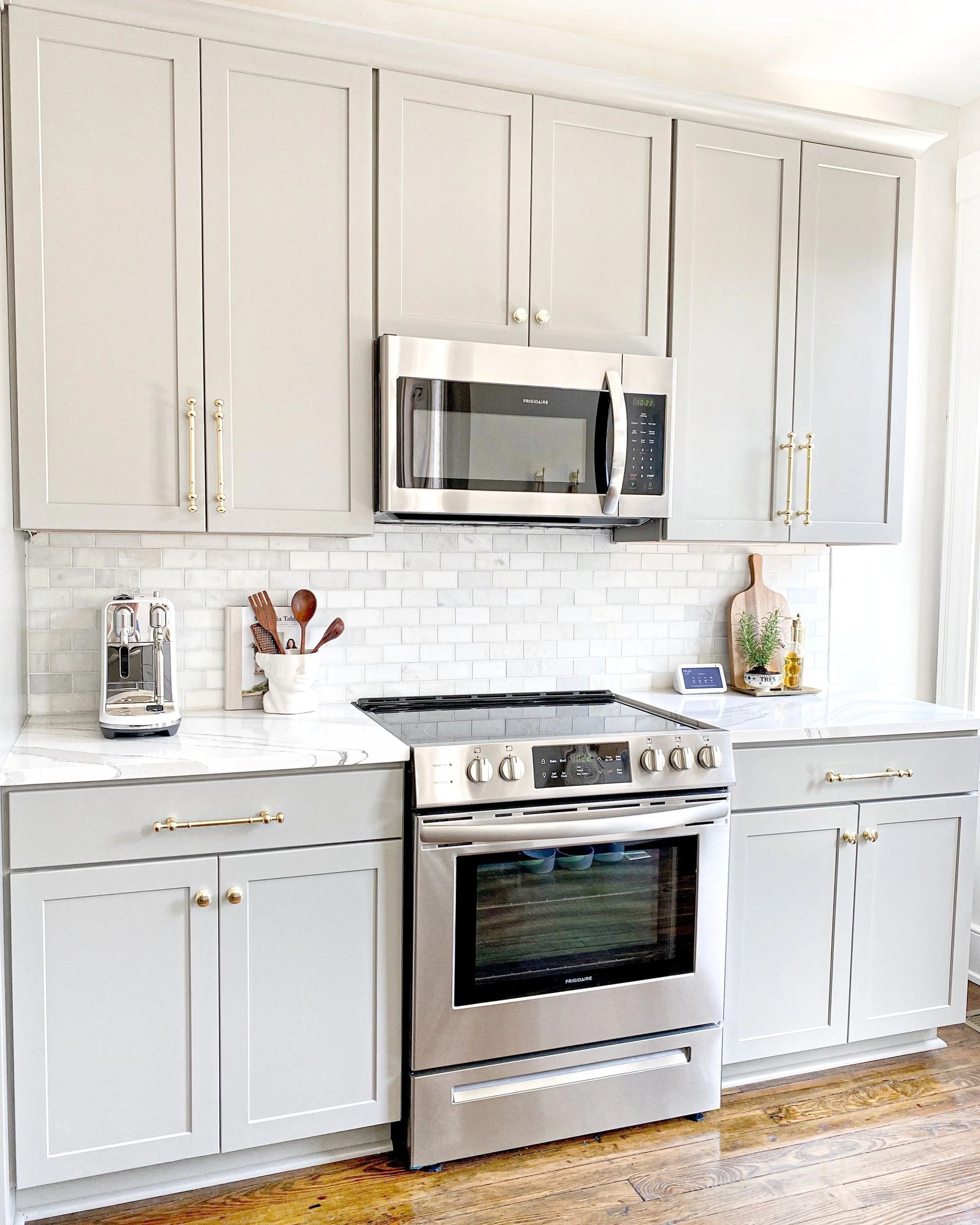 Bright white kitchen with stainless steel stove, microwave, and gray cabinets