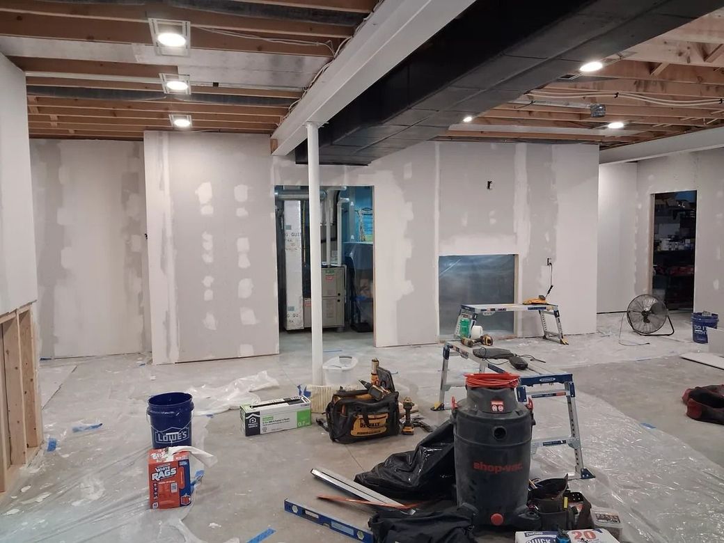 Basement under renovation with drywall, exposed beams, tools, and construction materials on the floor