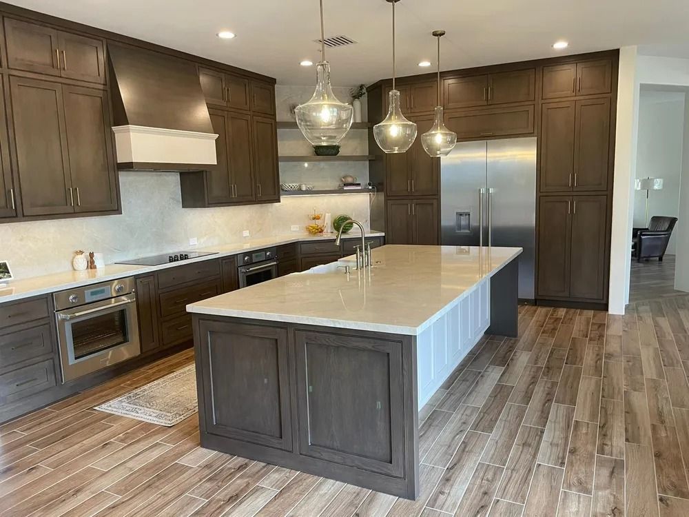 Modern kitchen with dark wood cabinets, large island, stainless steel appliances, and wood-look flooring