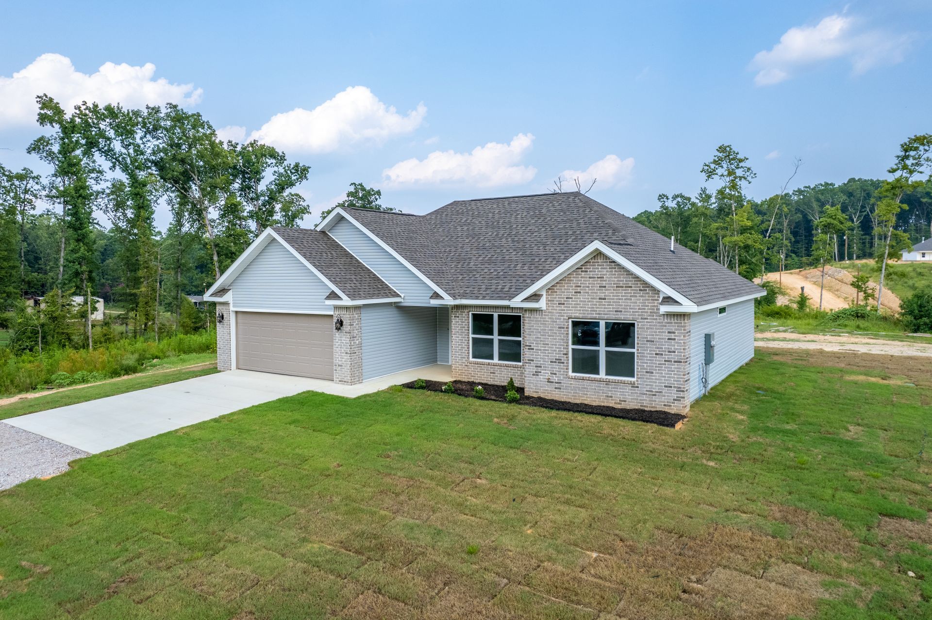 A one-story house with gray siding, a gray roof, and a concrete driveway on a grassy lot.