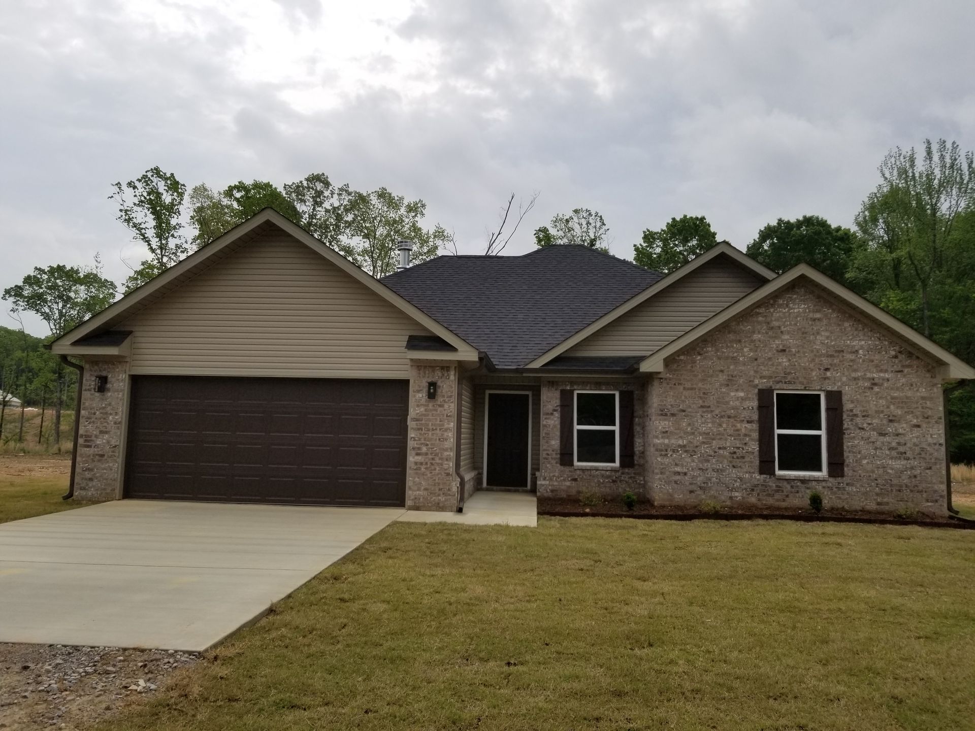 Brick house with brown garage door, shutters, and roof, on a cloudy day.