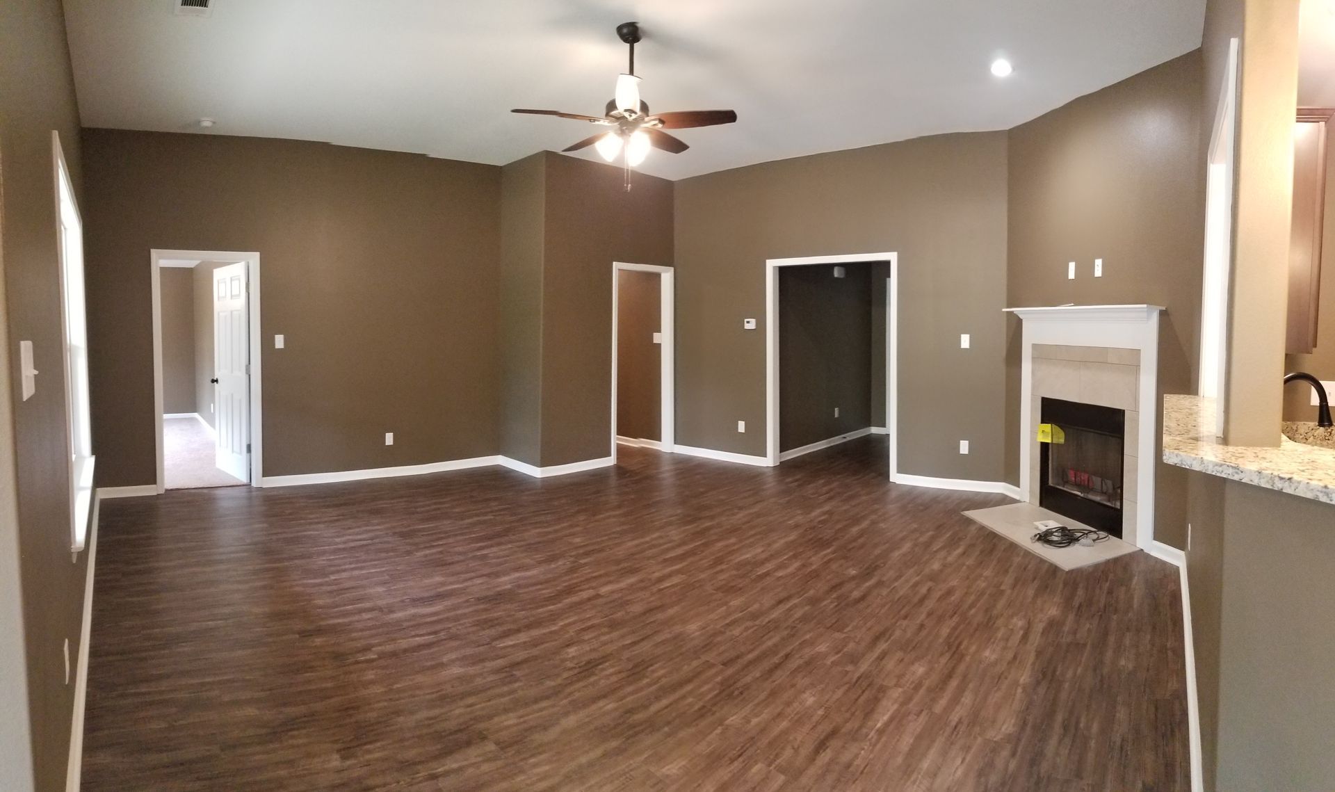 Brown-painted living room with wood-look flooring, multiple doorways, a fireplace, and a ceiling fan.