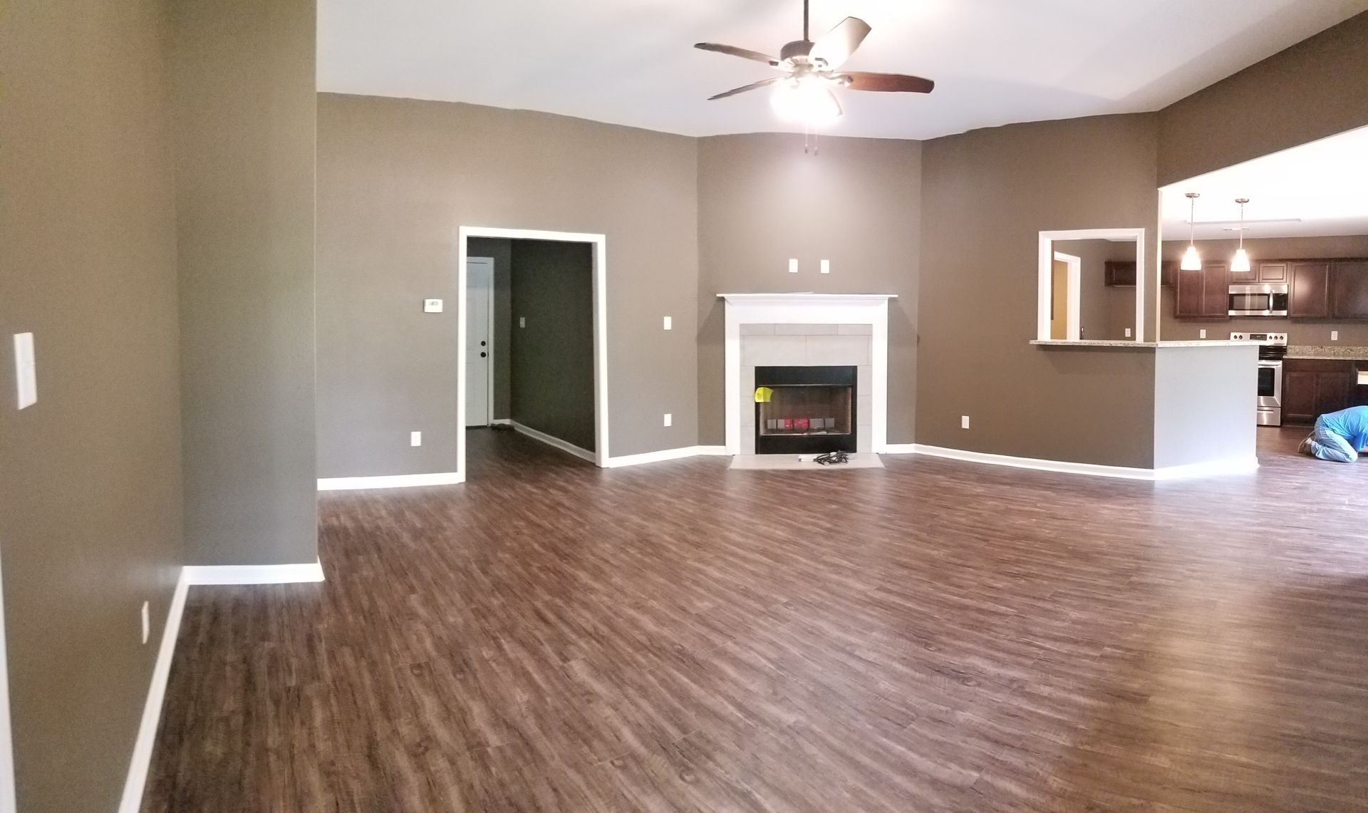 Empty living room with brown walls, wood floors, and fireplace.
