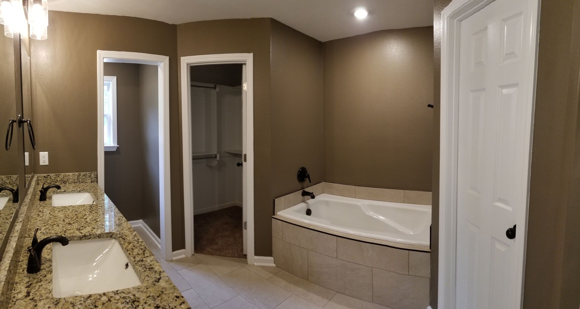 Bathroom with dual sinks, a tub, and a door to a closet, all in neutral colors with granite countertops.