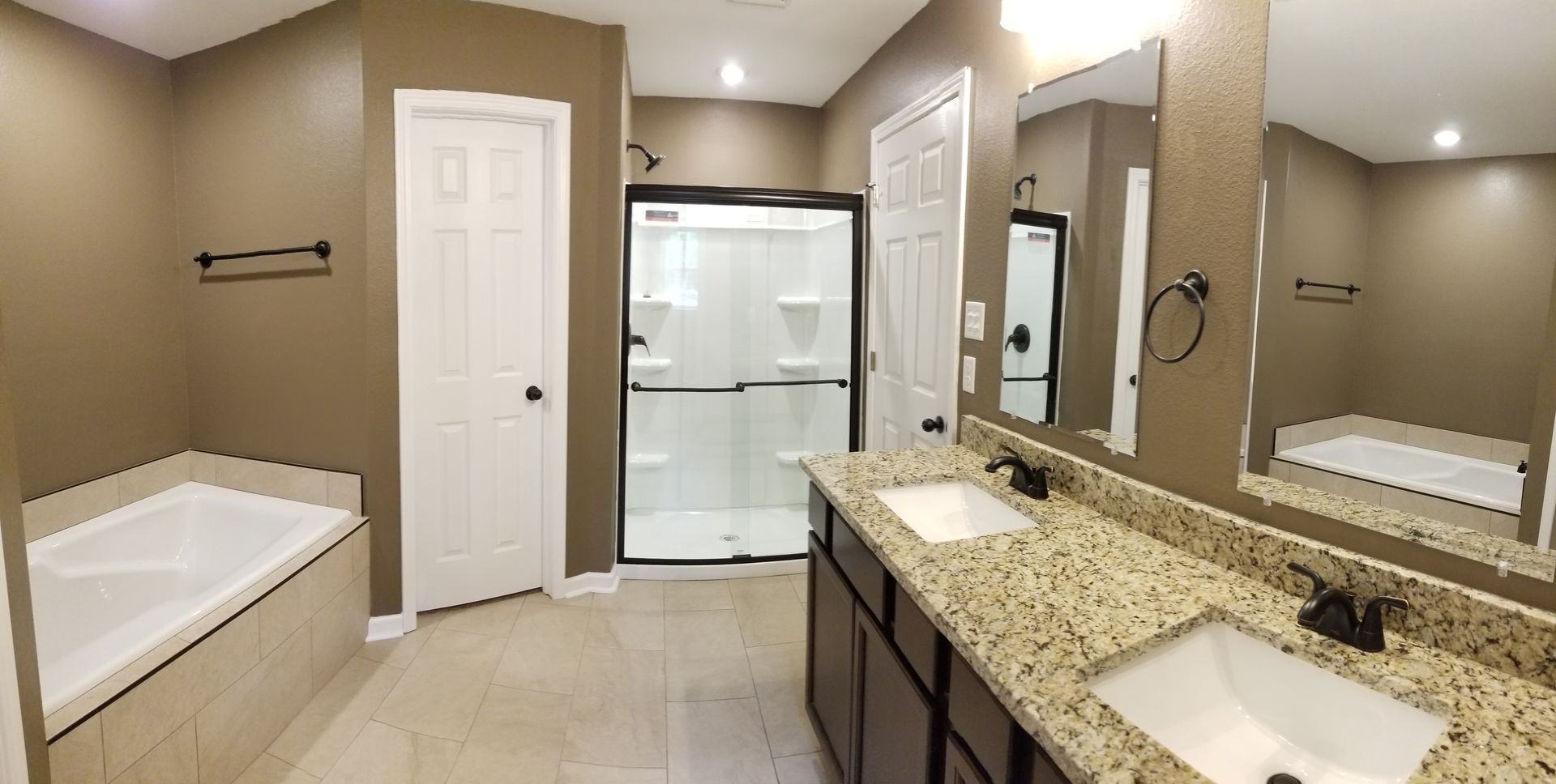 Bathroom with a bathtub, shower, double vanity, and brown walls.