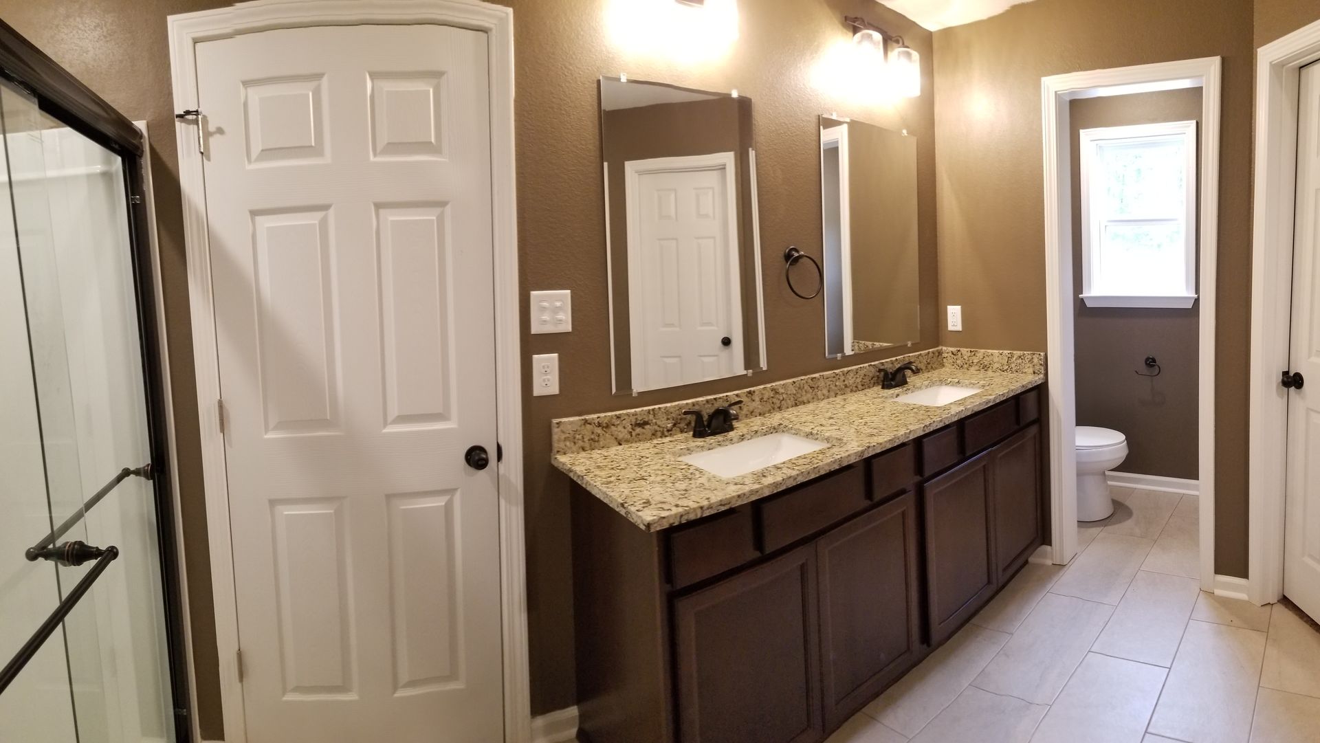 Bathroom with double vanity, brown cabinets, tan countertop, toilet, and shower.