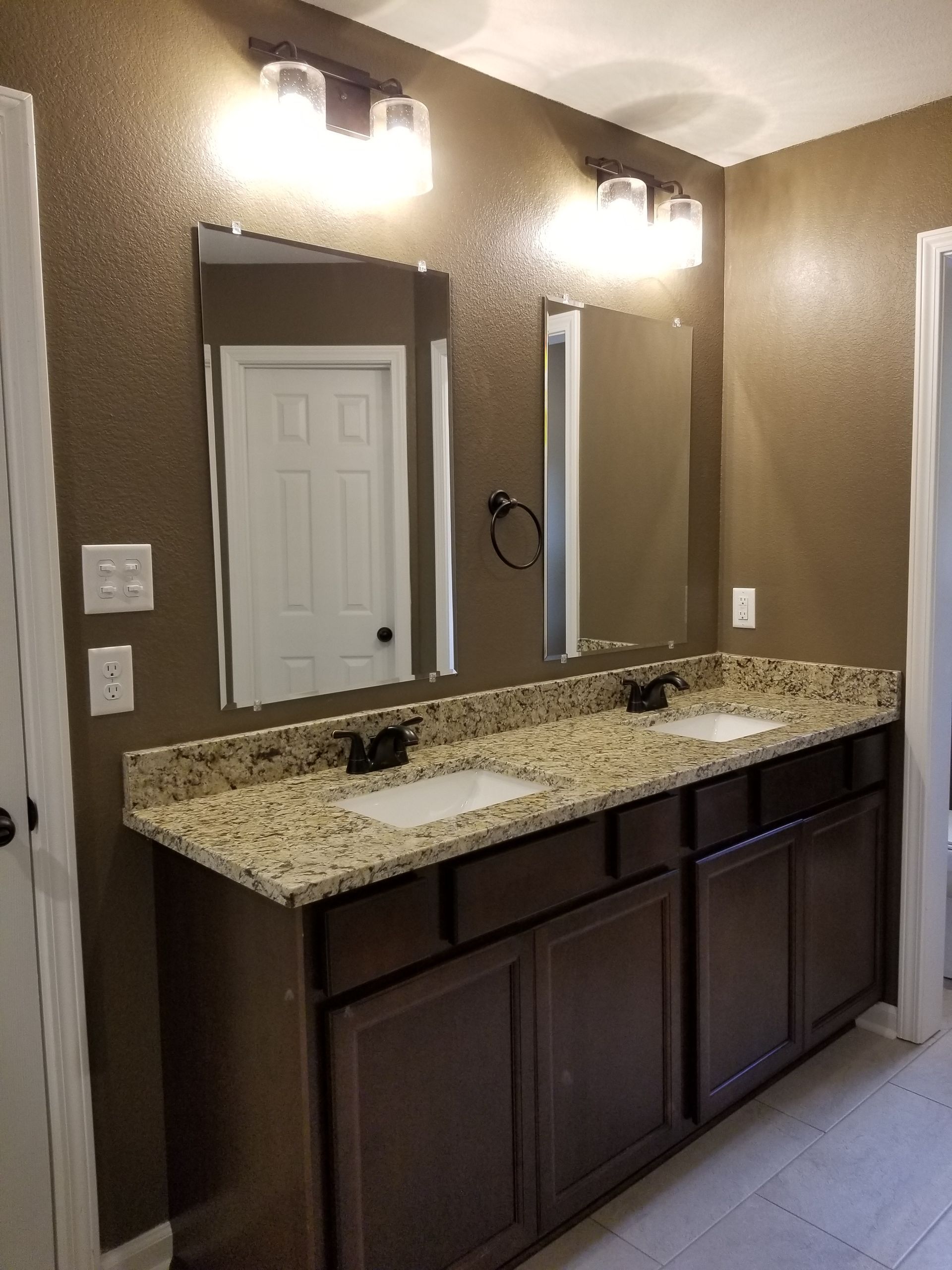 Bathroom with double vanity, brown cabinets, granite countertop, and brown walls.