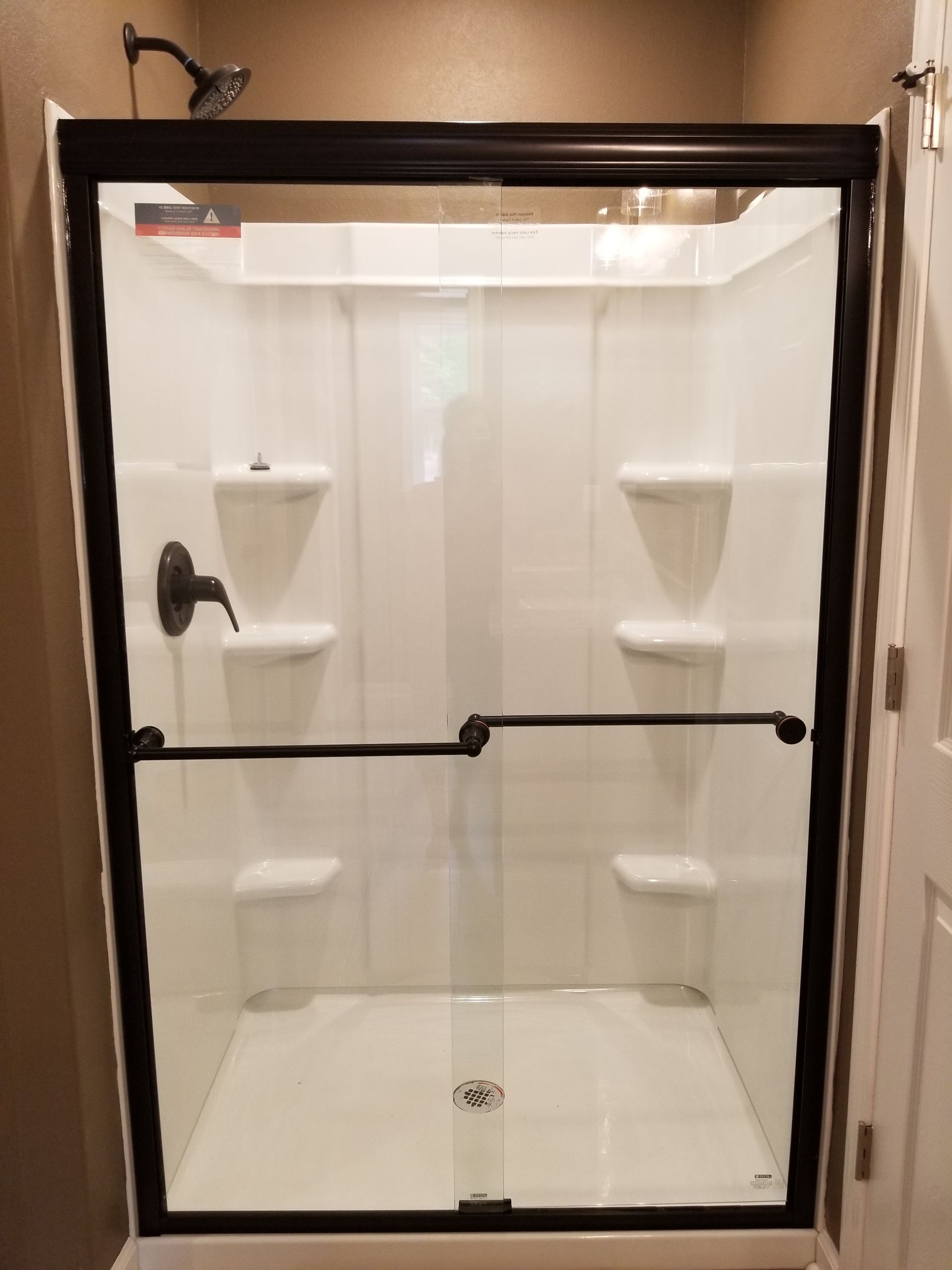 Black-framed white shower stall with glass doors, black hardware, and built-in shelves.