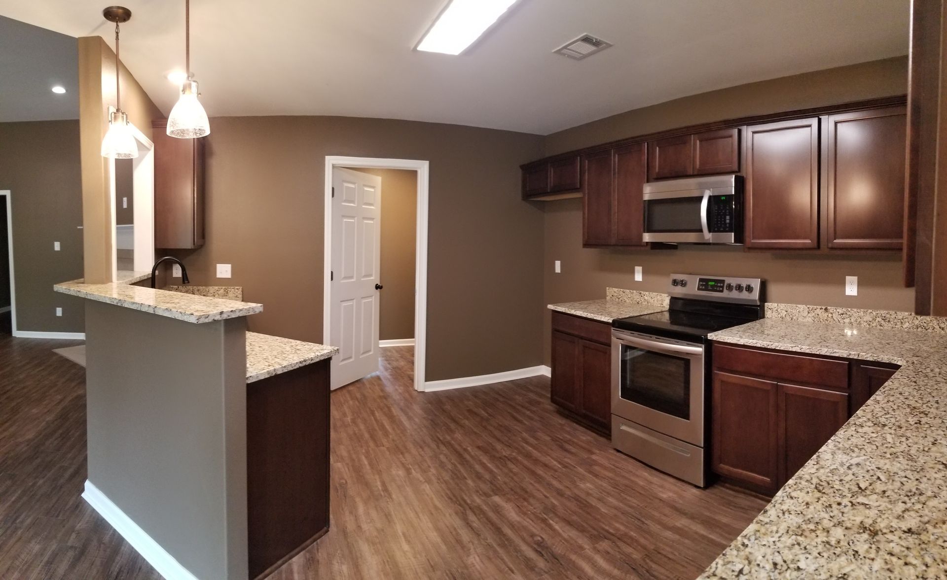 Kitchen with brown cabinets, granite countertops, and stainless steel appliances; wood-look flooring.
