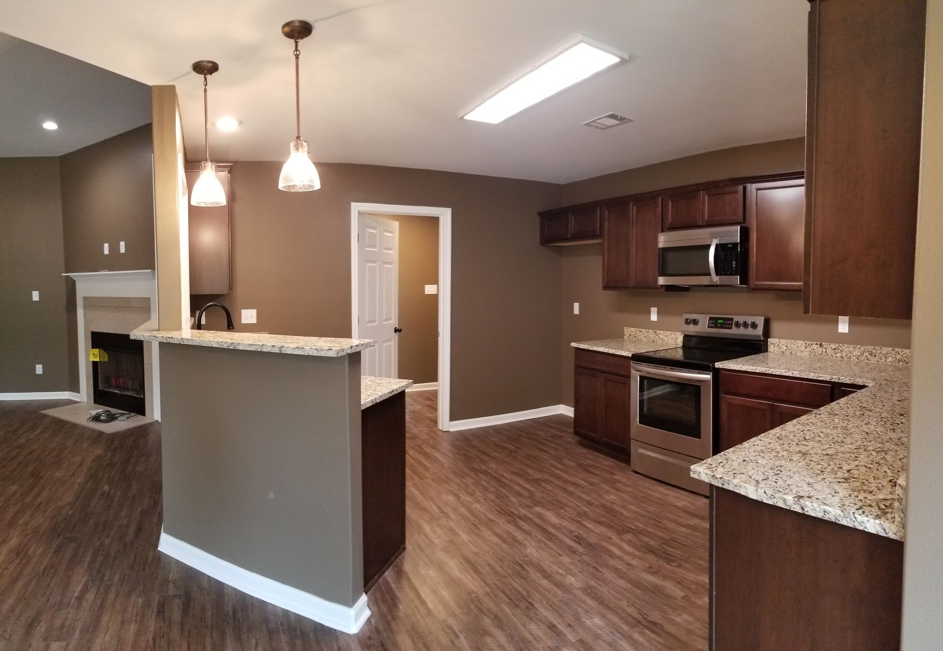 Kitchen with dark brown cabinets, granite counters, and pendant lights.