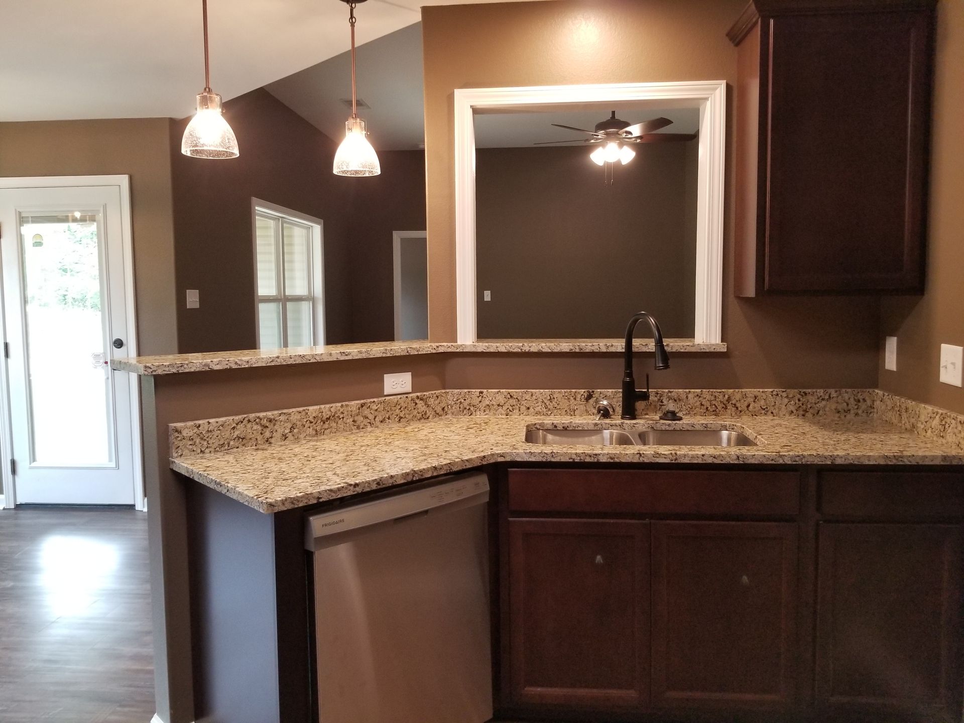 Kitchen with dark brown cabinets, granite countertop, dishwasher, and pendant lights.