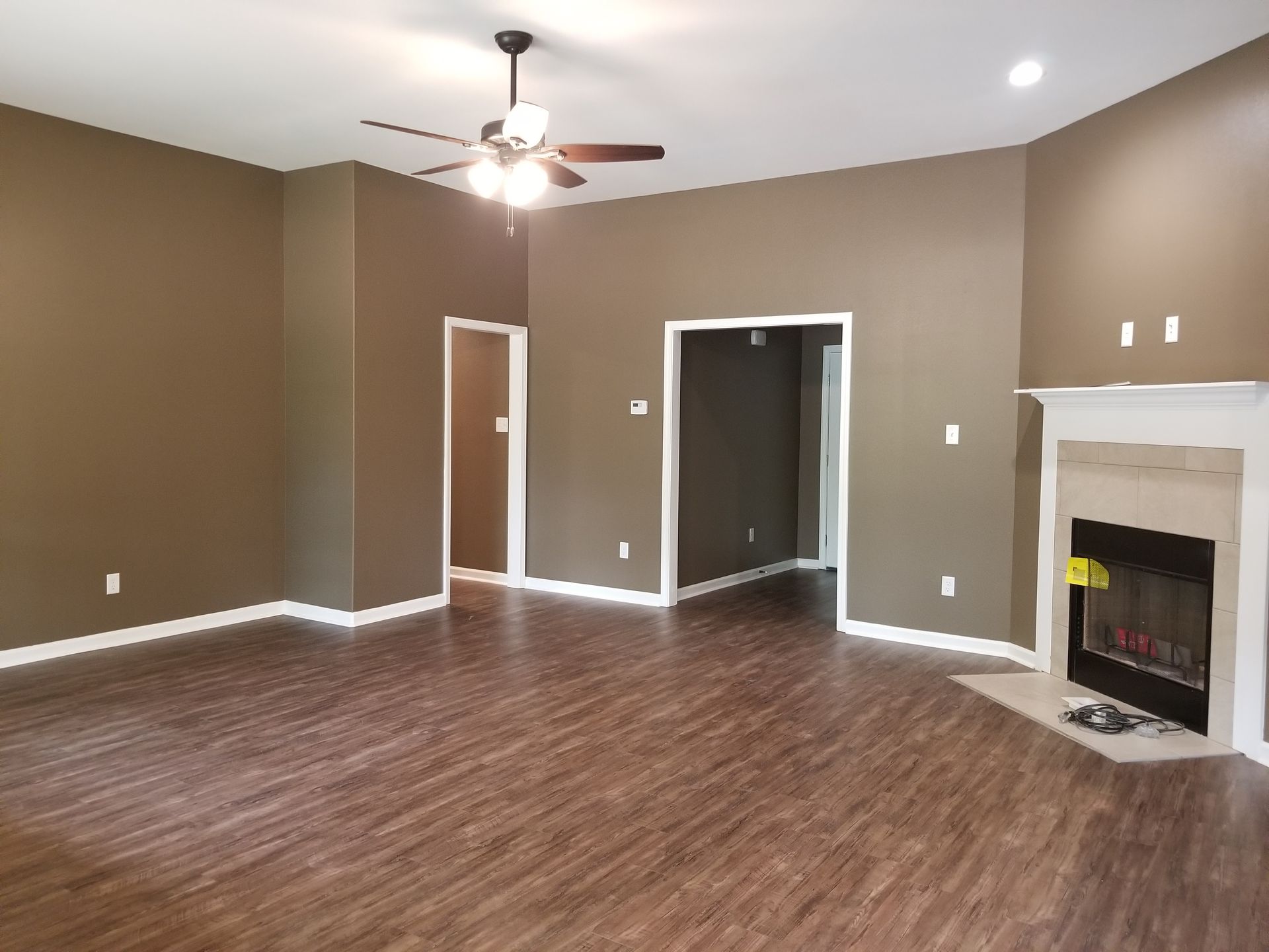 Living room with brown walls, wood floors, fireplace, and ceiling fan.