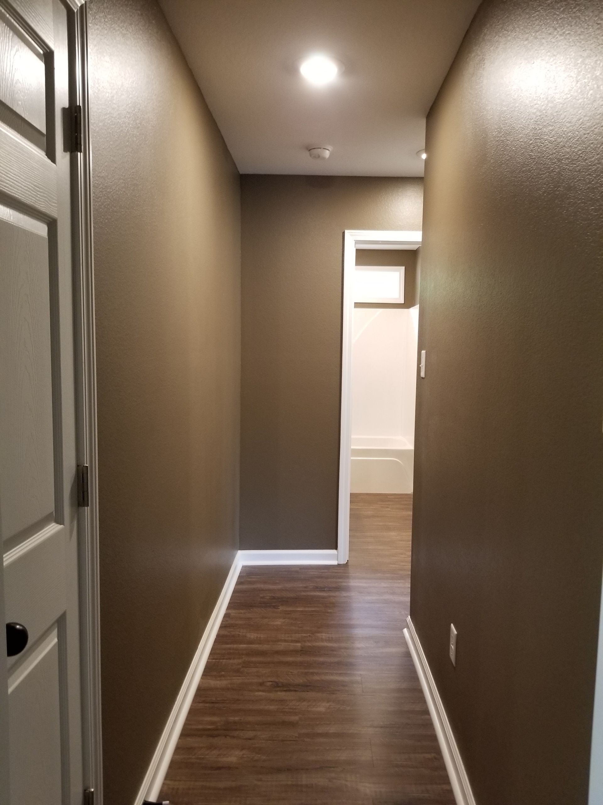 Brown hallway with white trim and doors, leading to a white doorway.