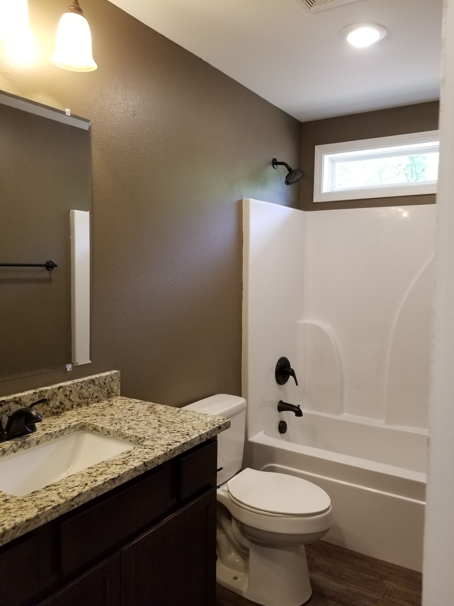 Bathroom with a brown wall, white tub, toilet, and granite countertop vanity.