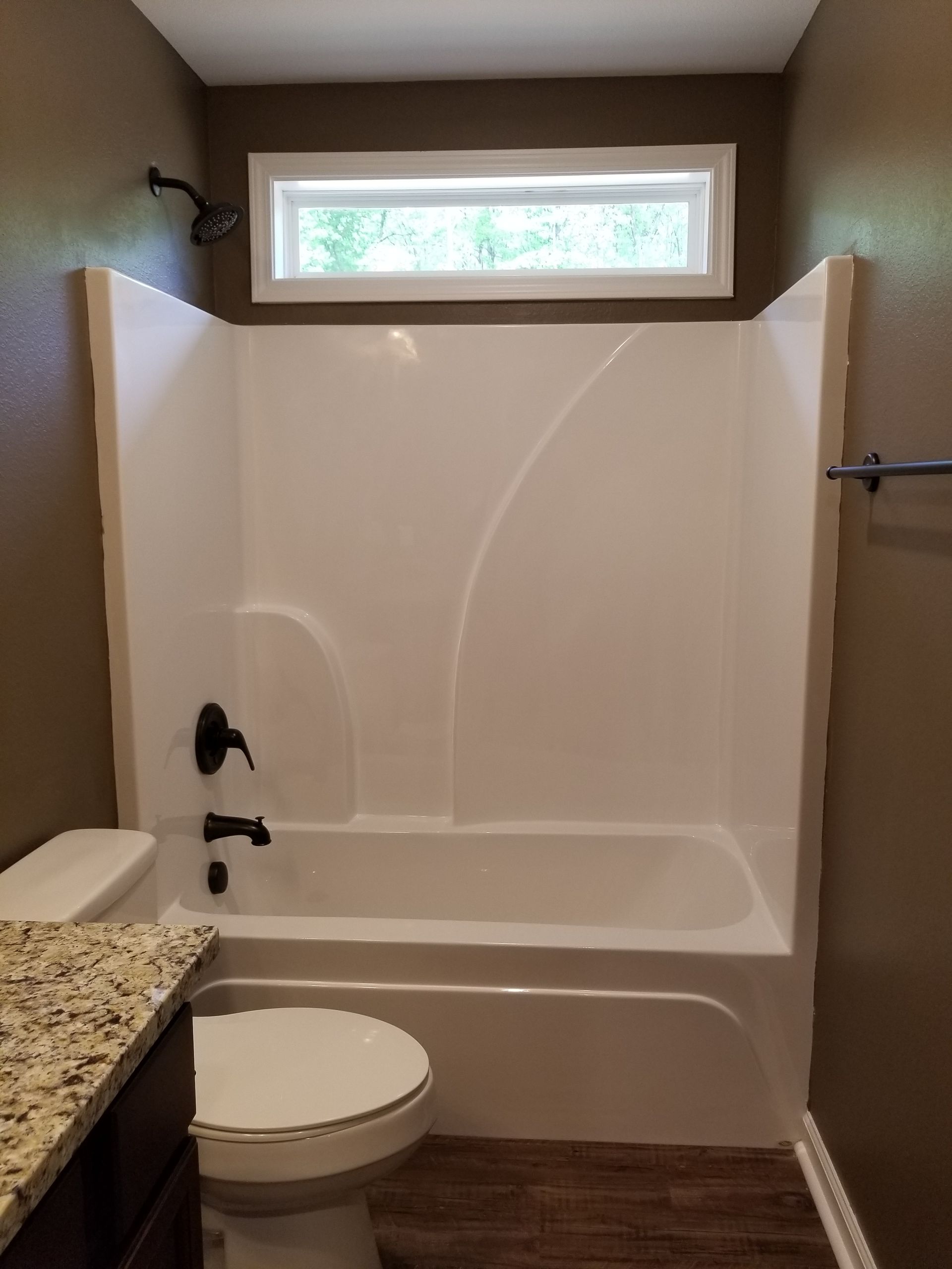 Bathroom with white tub, brown walls, toilet, and window.