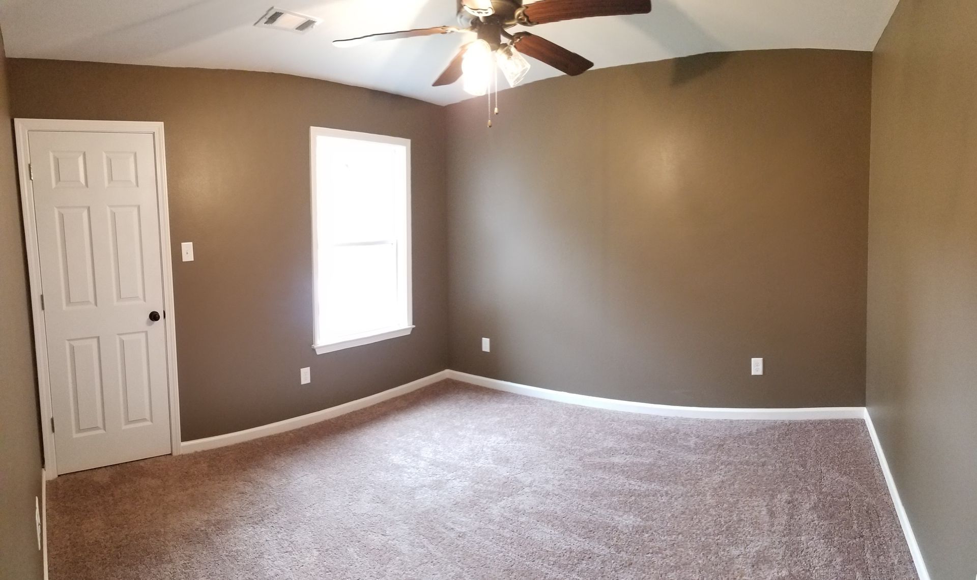 Bedroom with brown walls, white door and window, brown carpet, ceiling fan.