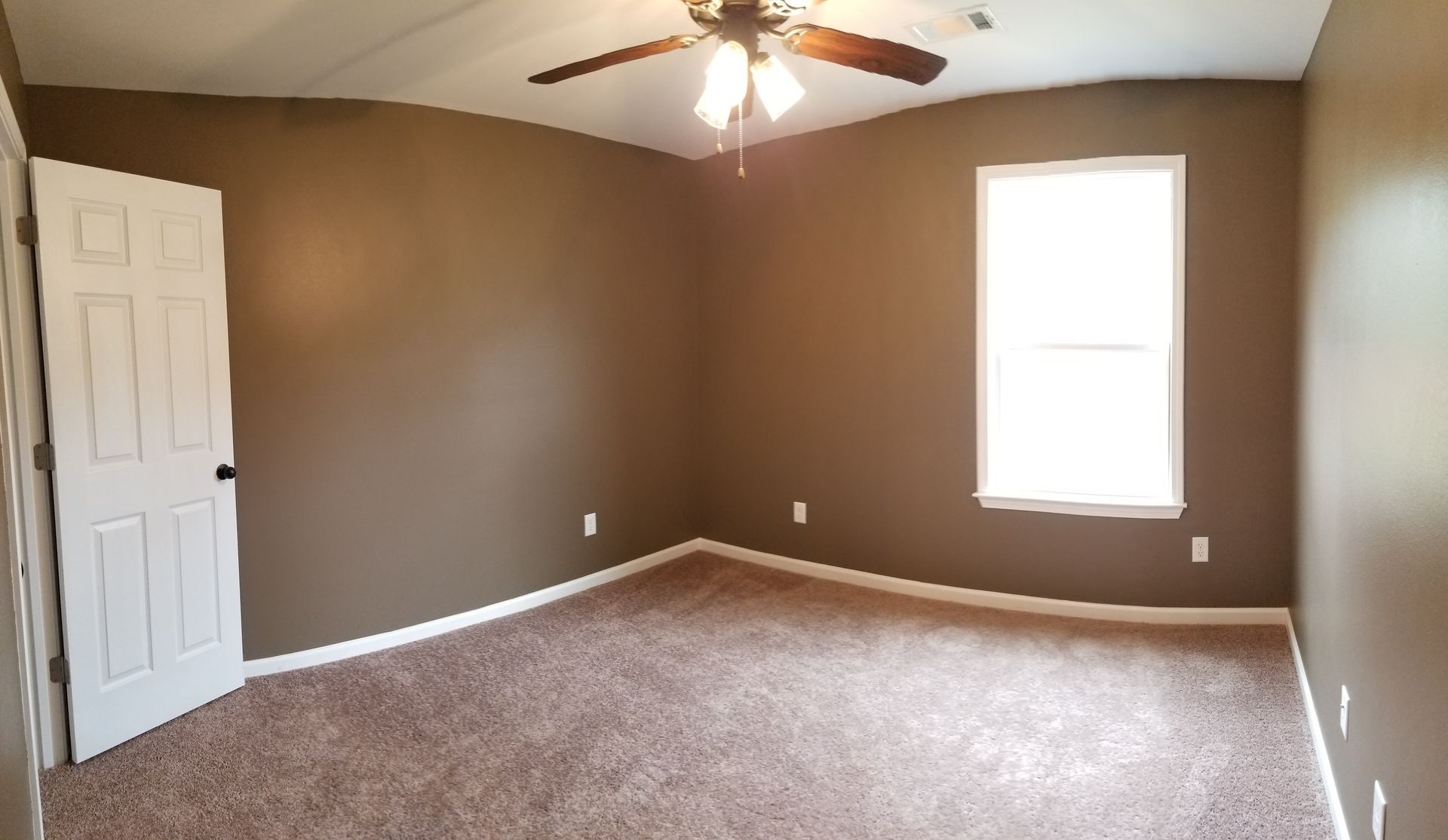 Empty bedroom with brown walls, carpet, white door/window frame, ceiling fan.