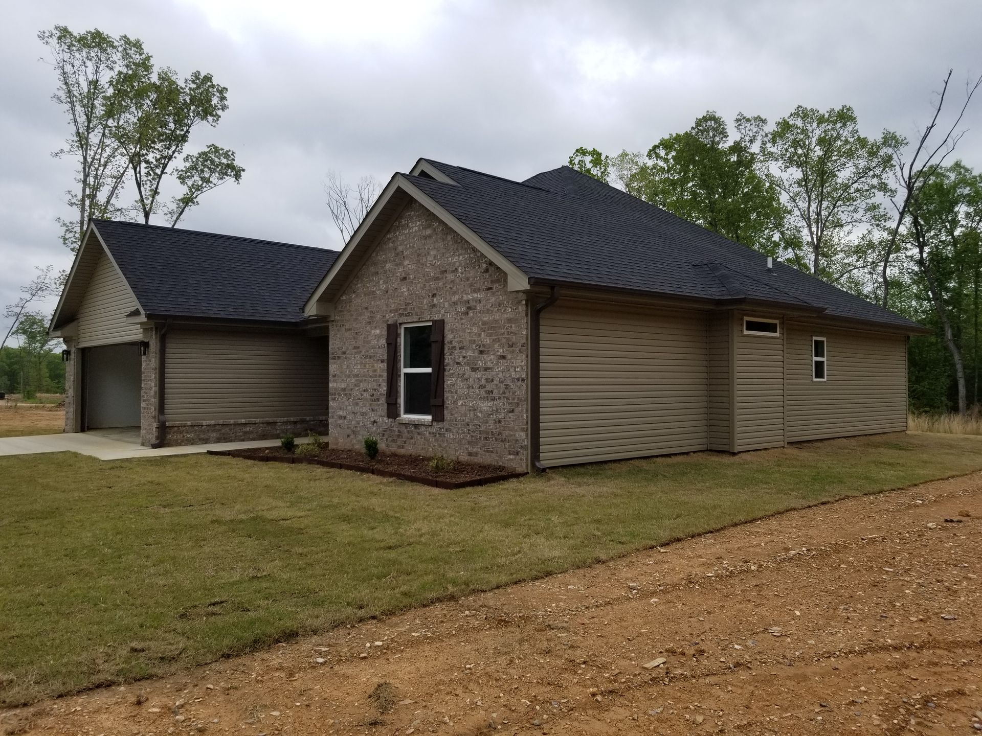 New brick and tan siding house with black roof and garage on overcast day.