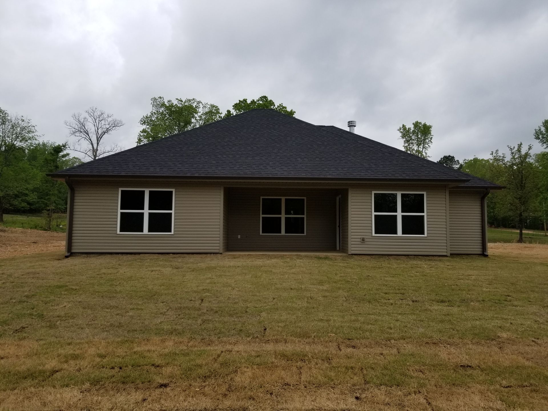 Tan house with dark roof and windows, set on a grassy lot.