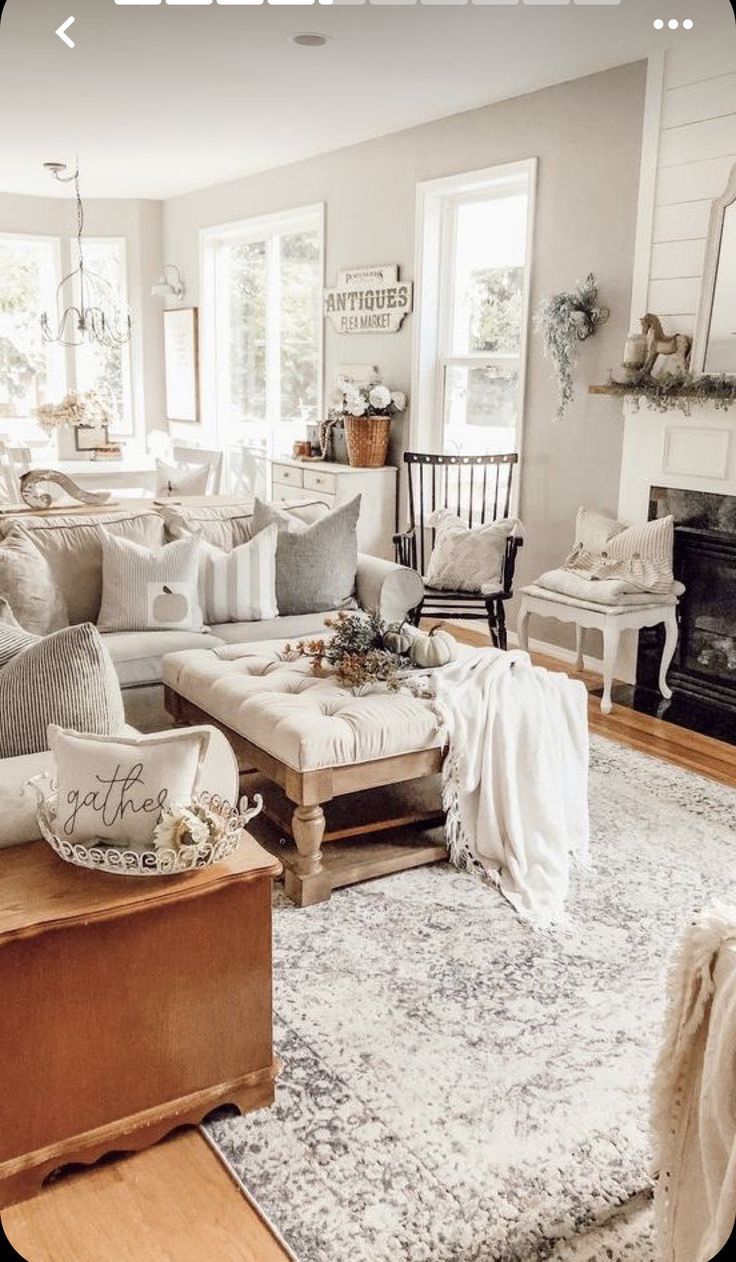 Cozy living room with a light-colored rug, white couch, and fireplace. Decorated with pillows, a wooden trunk, and plants.