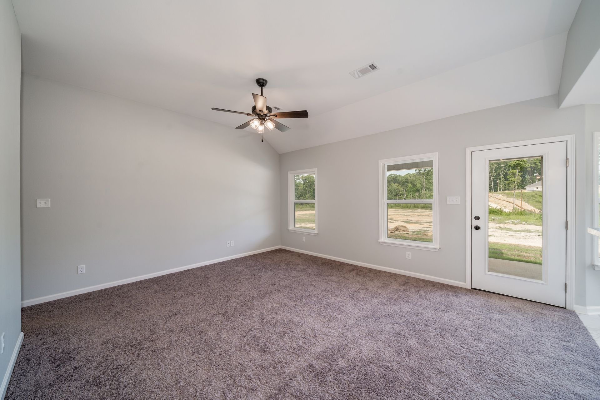 Empty room with gray walls, brown carpet, windows, and a door to the outdoors.