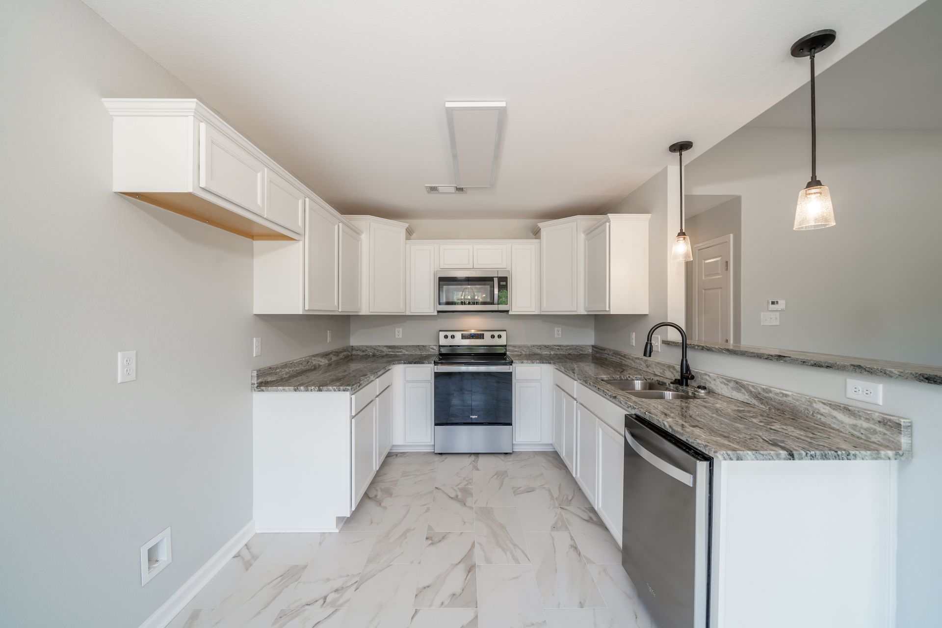 White kitchen with granite countertops, stainless steel appliances, and light gray walls.