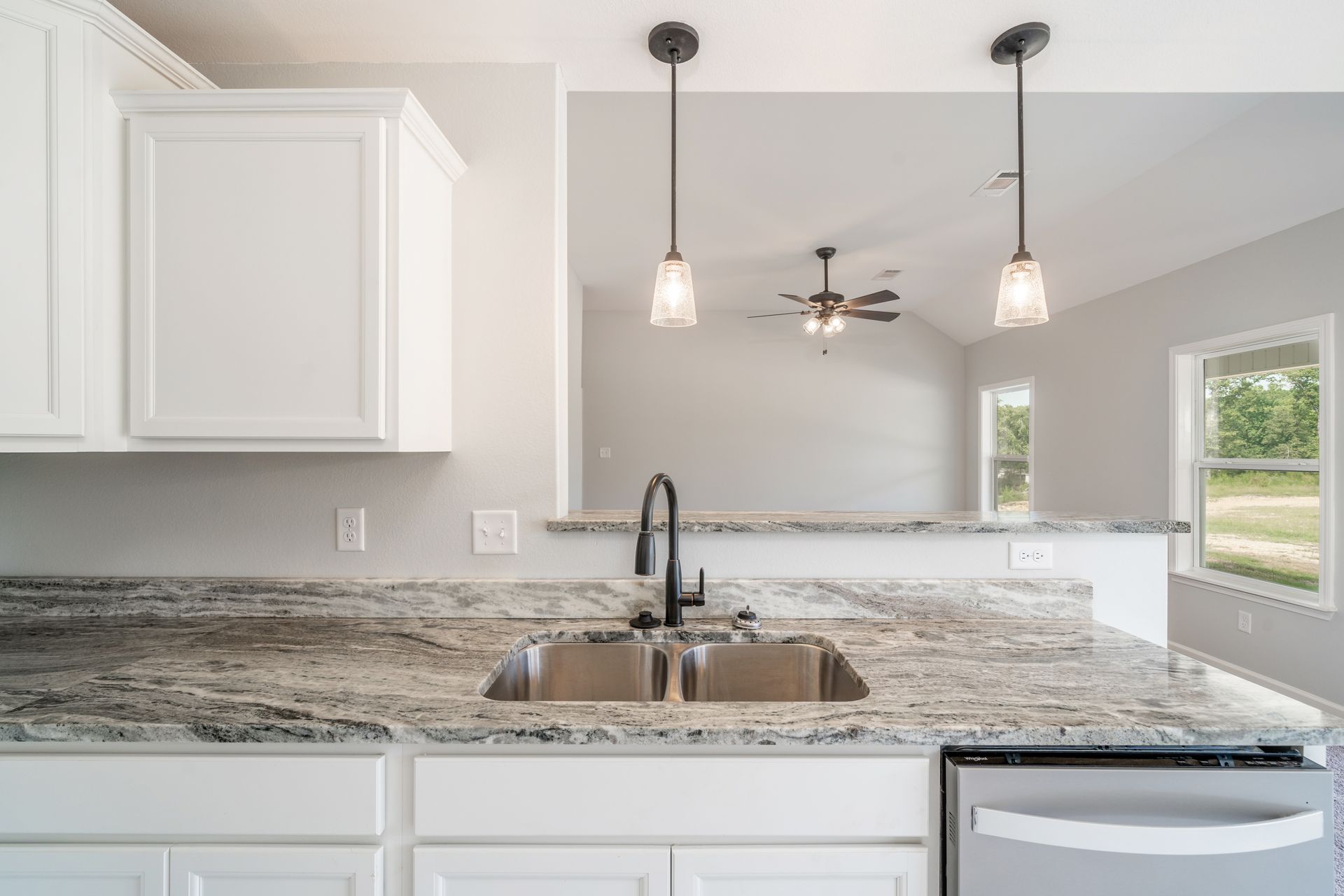 Kitchen with white cabinets, granite countertop, black faucet, and pendant lights; view into living area.