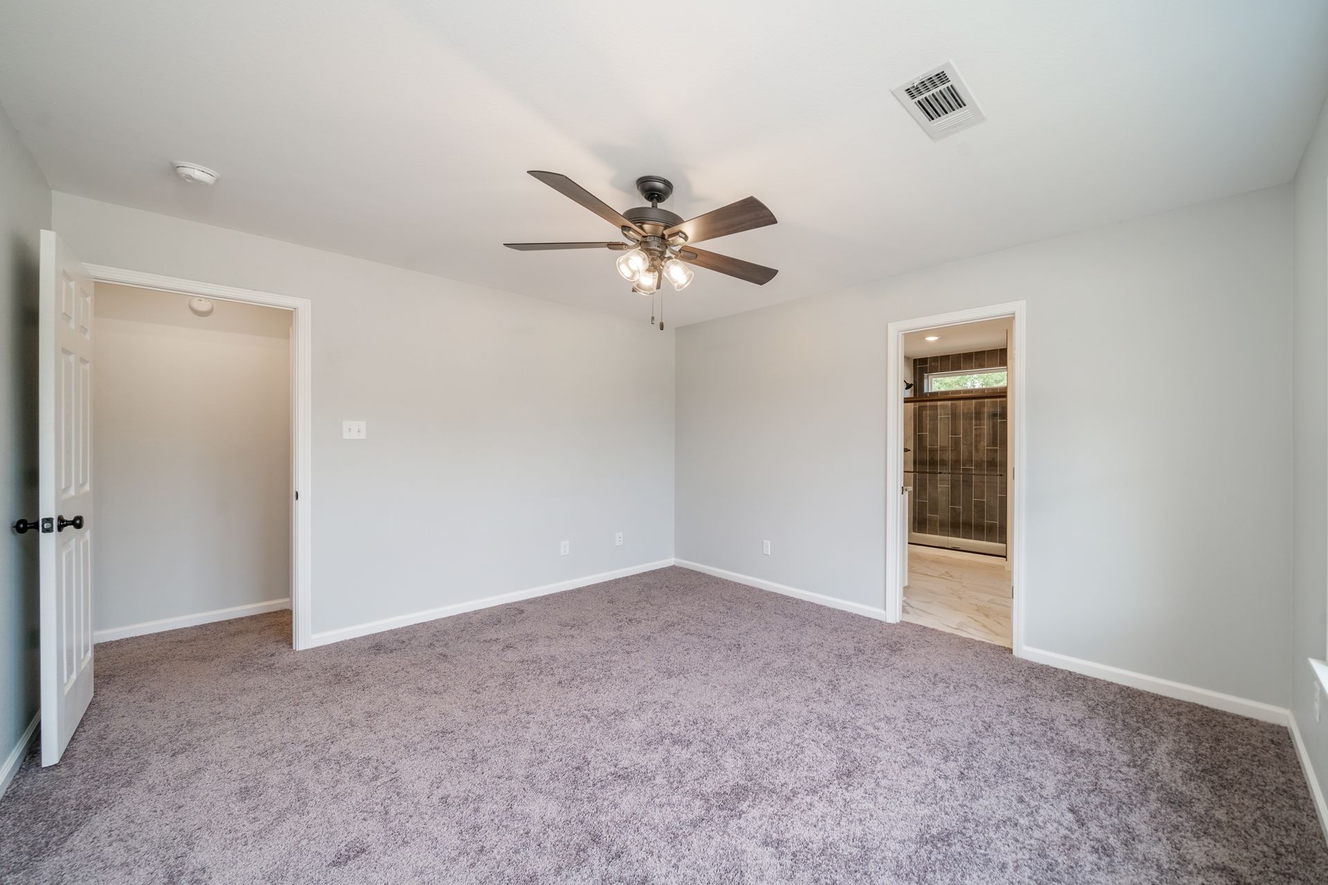 Bedroom with gray walls and carpet; a ceiling fan hangs from the ceiling.