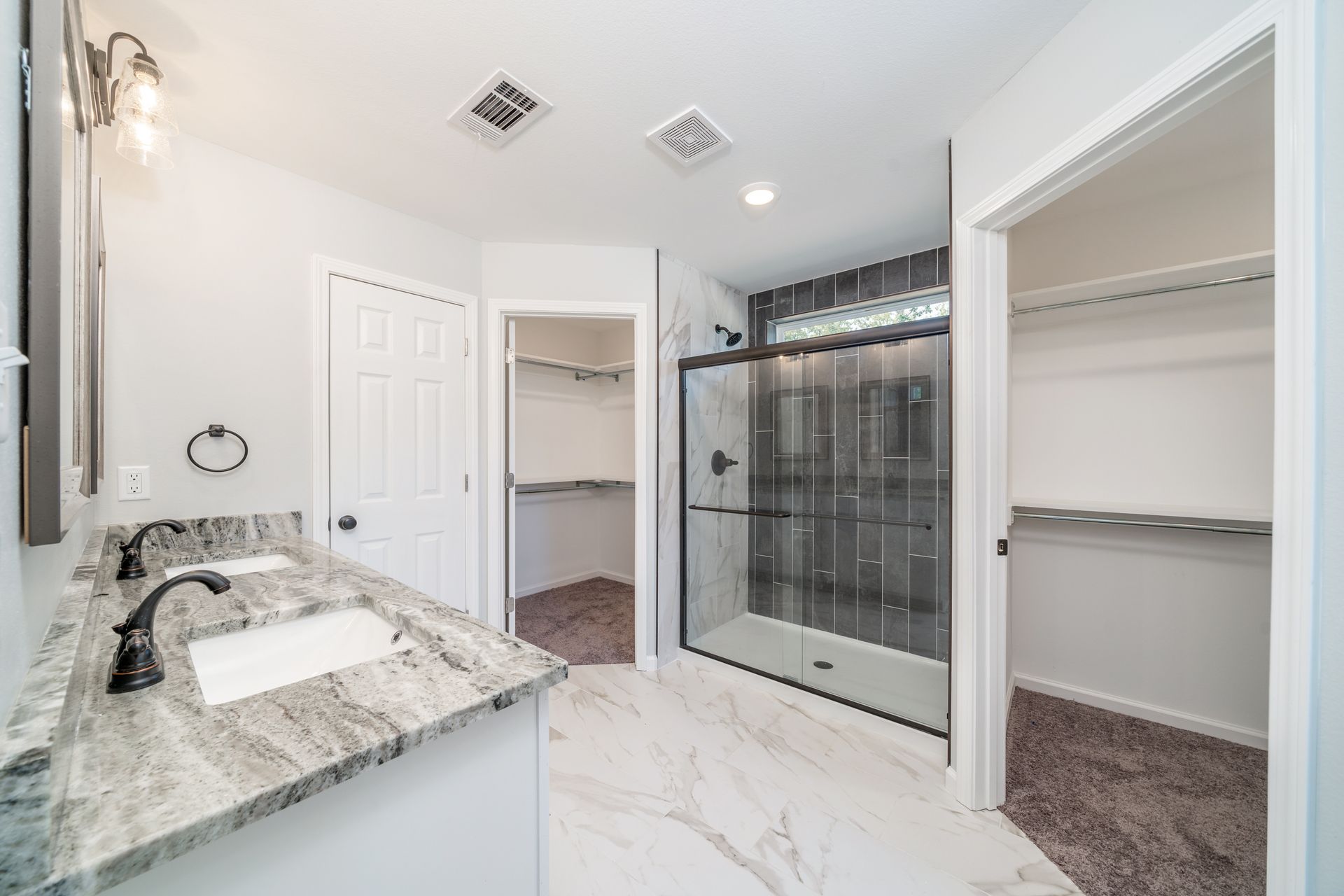 Bathroom with double vanity, walk-in shower, and two walk-in closets; light gray walls, marble-look floor.