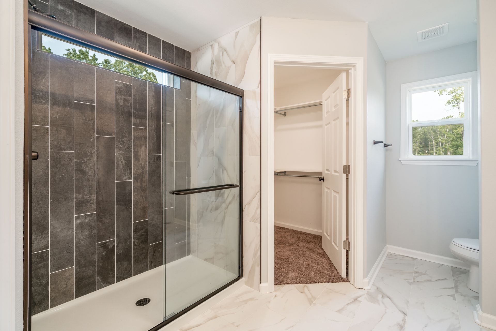 Bathroom with a glass shower, walk-in closet, and a window. The floor is marble-like, with light gray walls.