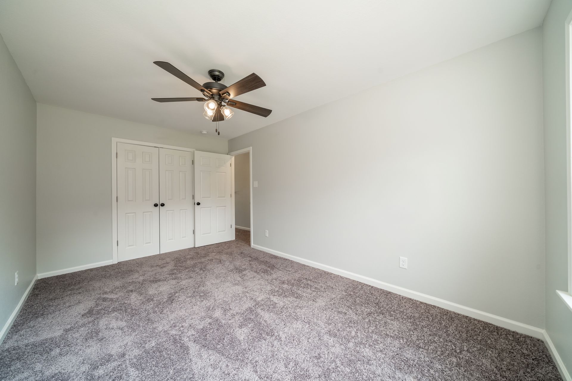 Empty bedroom with gray walls, carpet, closet, and a ceiling fan.
