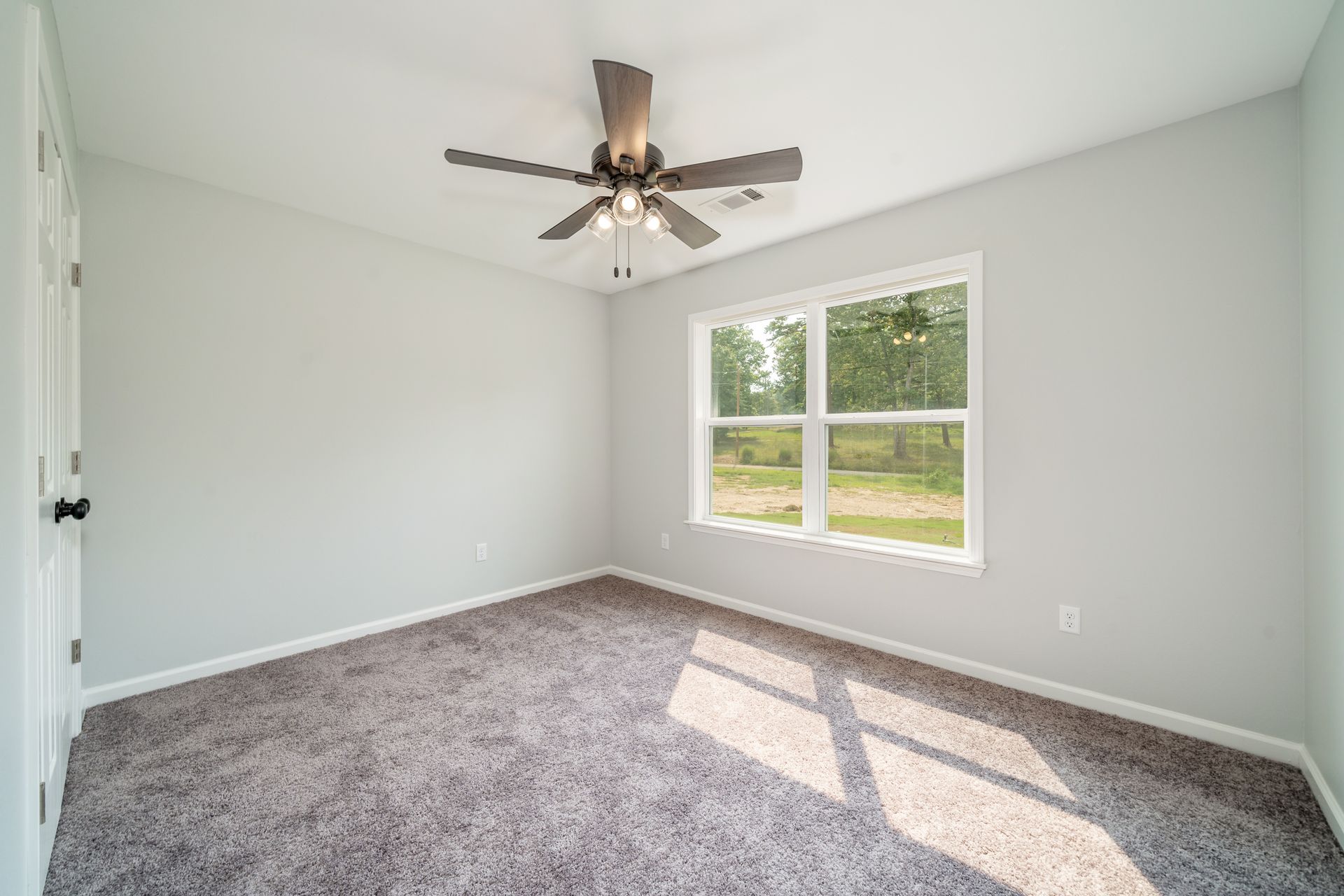 Empty bedroom with gray walls, carpet, window, and ceiling fan.