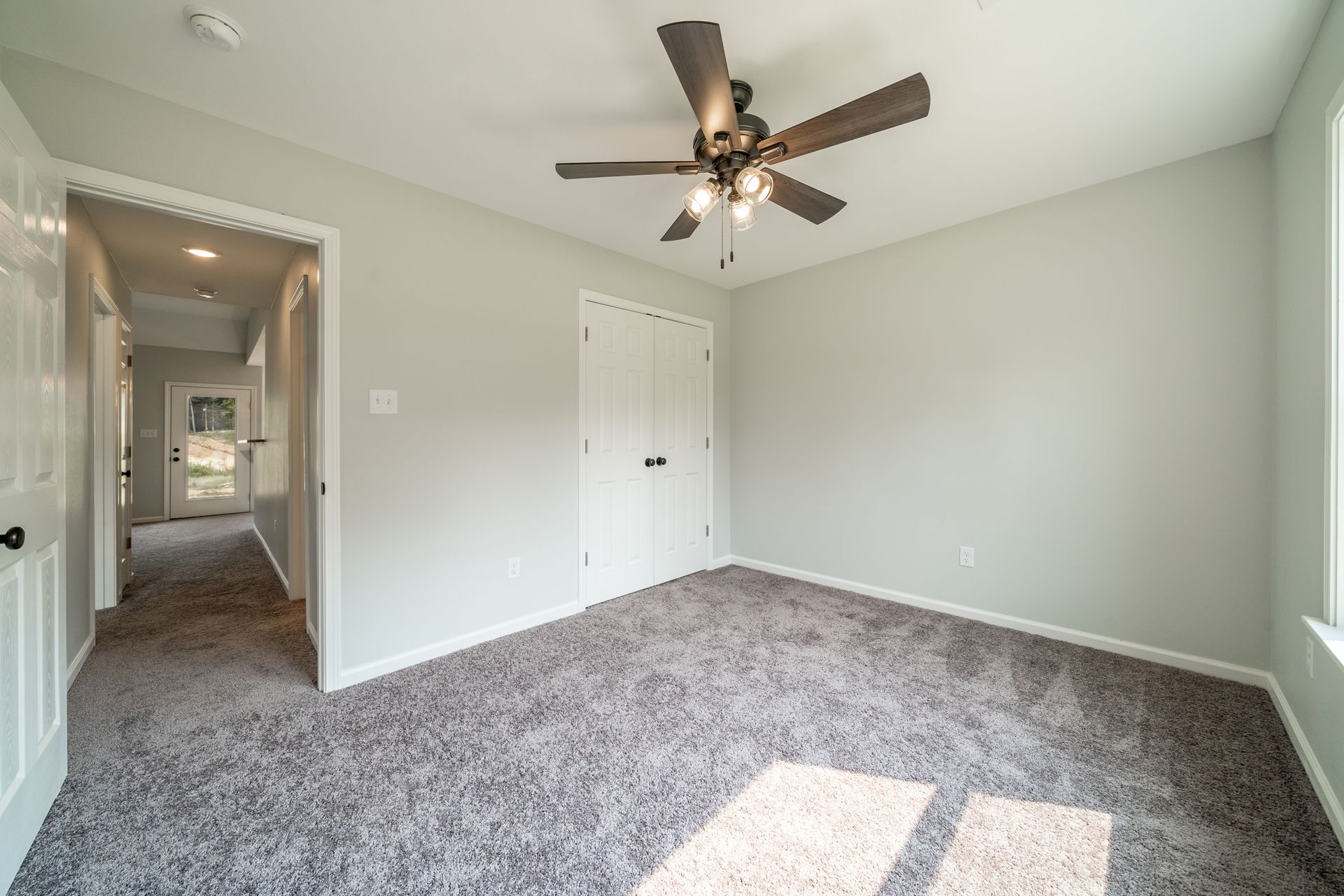 Empty bedroom with grey carpet, light grey walls, white doors and trim, and a ceiling fan.