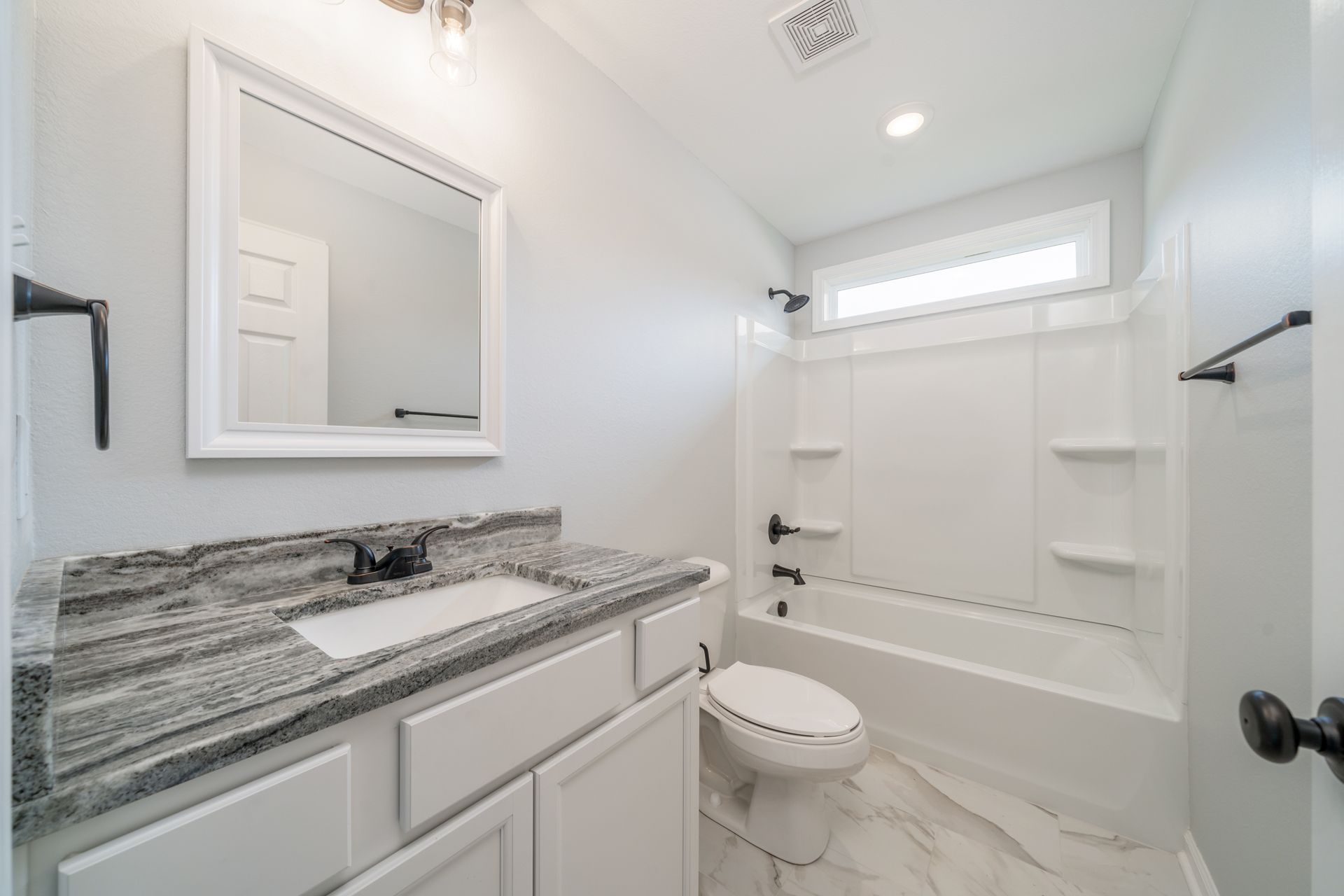 White bathroom with grey granite countertop, toilet, and bathtub.