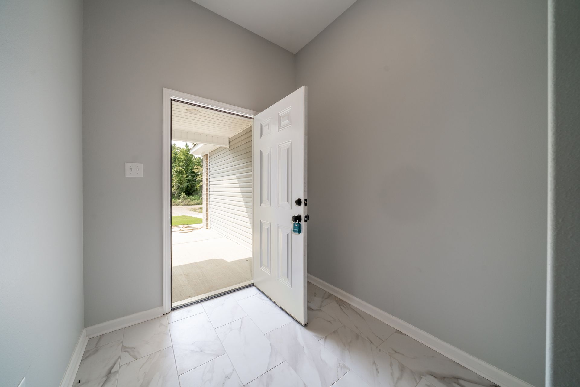 Interior doorway with white door open, revealing a porch and exterior; gray walls.