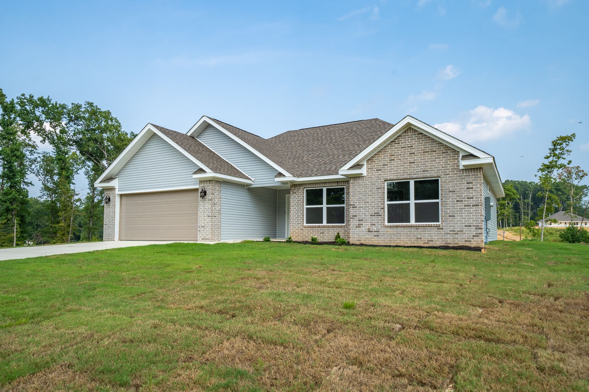 New brick home with gray roof and garage, on a green lawn under a blue sky.
