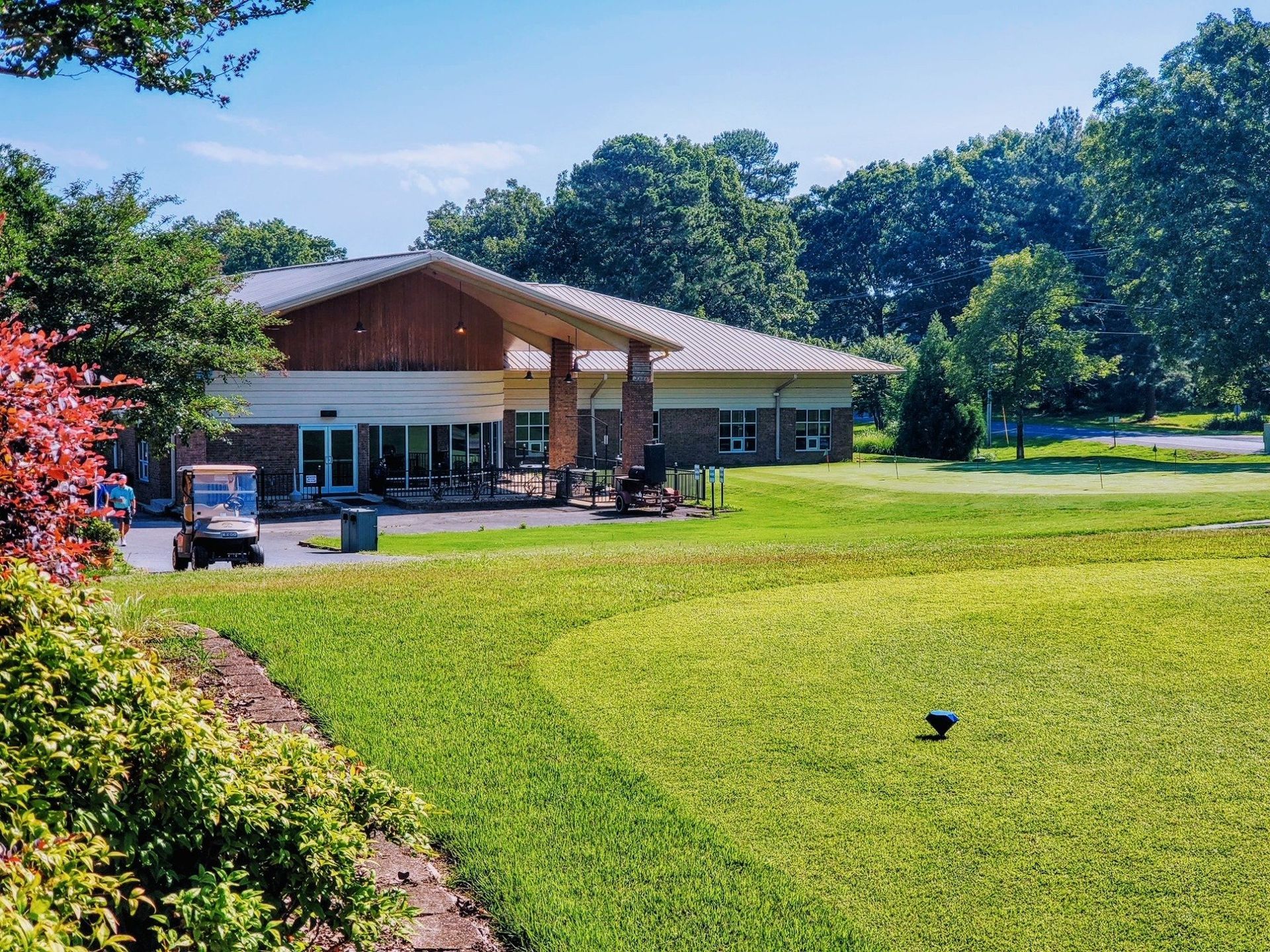 Golf course clubhouse with green grass, trees, and a golf cart on a sunny day.