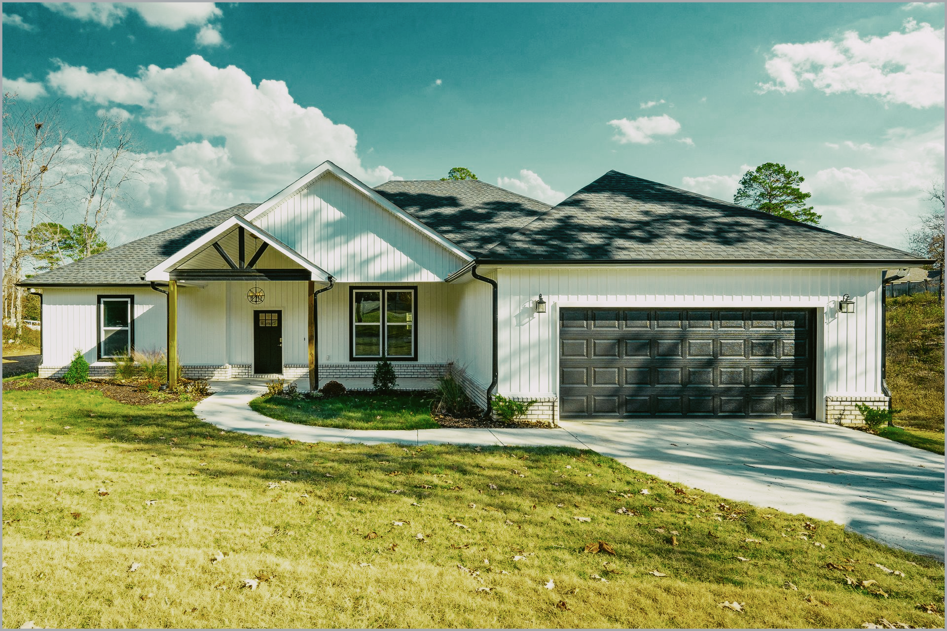 White farmhouse with black garage door and roof under a blue sky.
