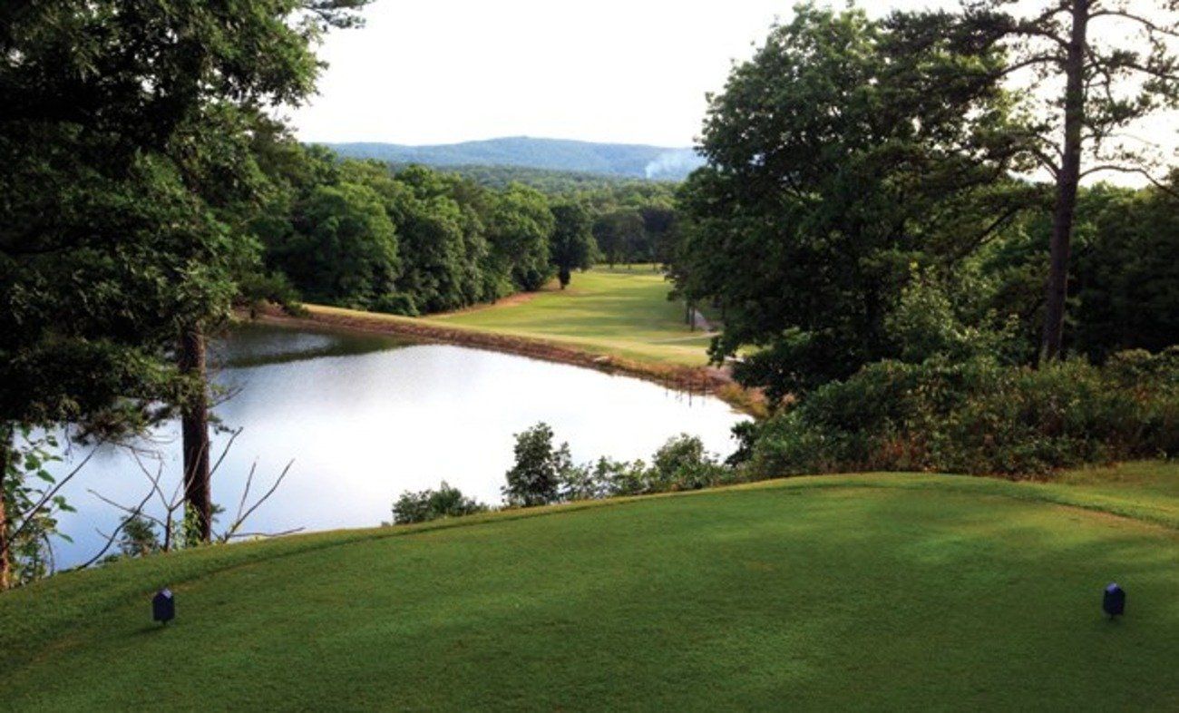 Golf course with a green tee box overlooking a pond and fairway lined by trees.