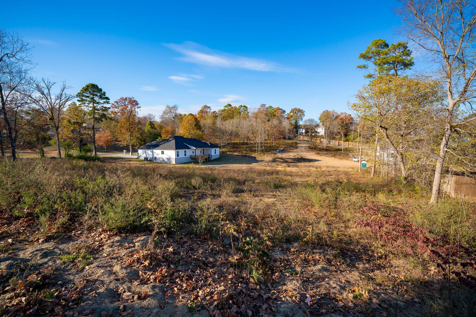 White house in a field, surrounded by trees with fall foliage, under a blue sky.