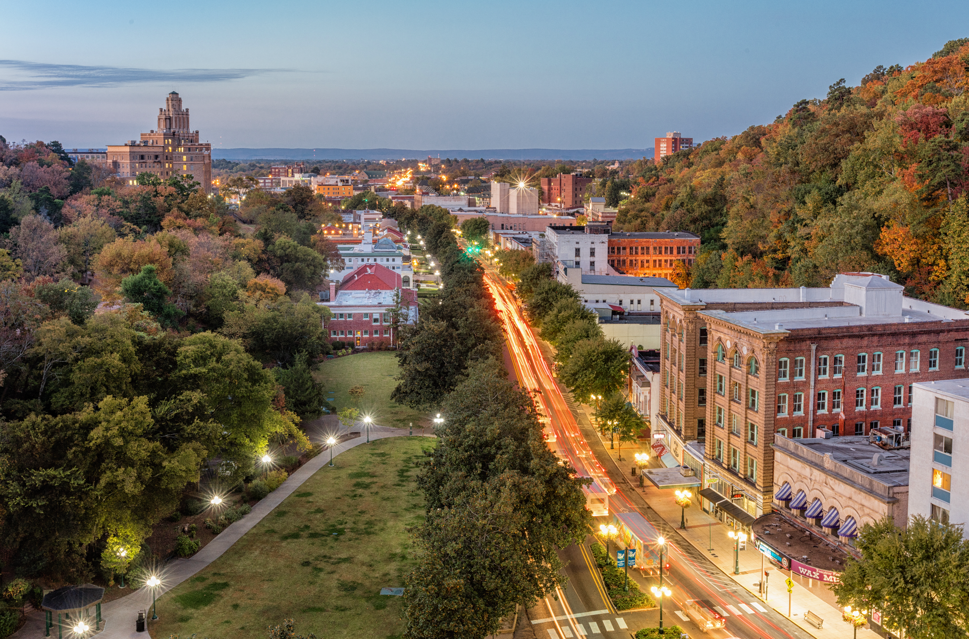 A city street lined with trees, buildings, and streetlights at dusk.