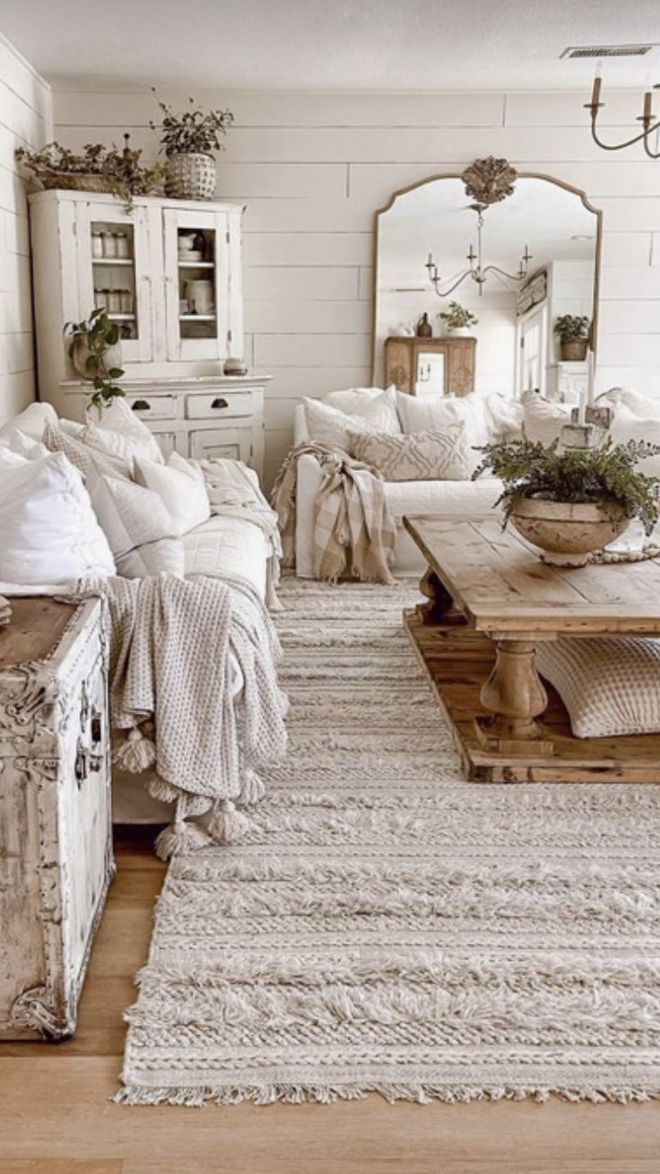 Cozy living room with white furniture, weathered wood coffee table, large mirror, and textured rug.
