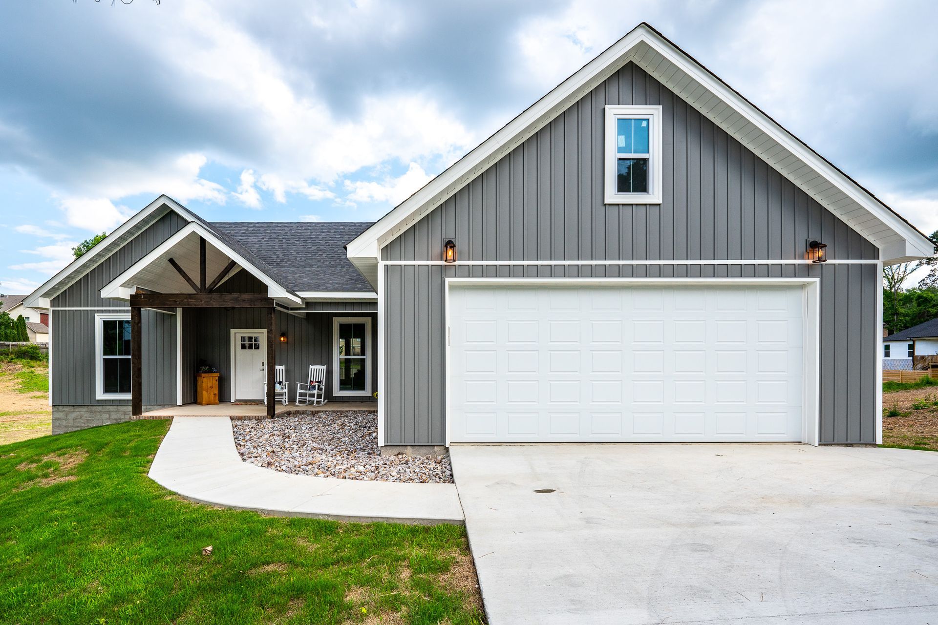 Gray house with a white garage door and a concrete driveway on a cloudy day.