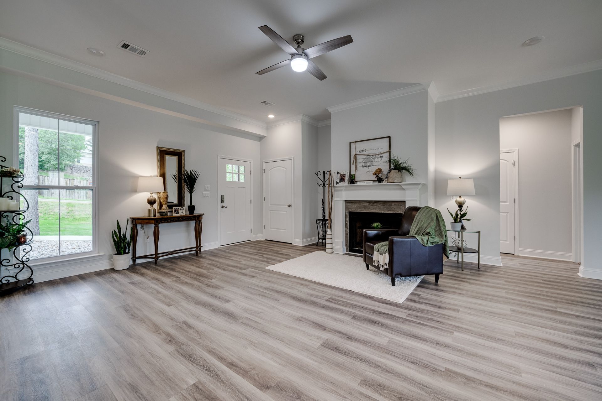 Spacious living room with hardwood floors, white walls, and a fireplace. Furnished with tables, chairs, and lamps.