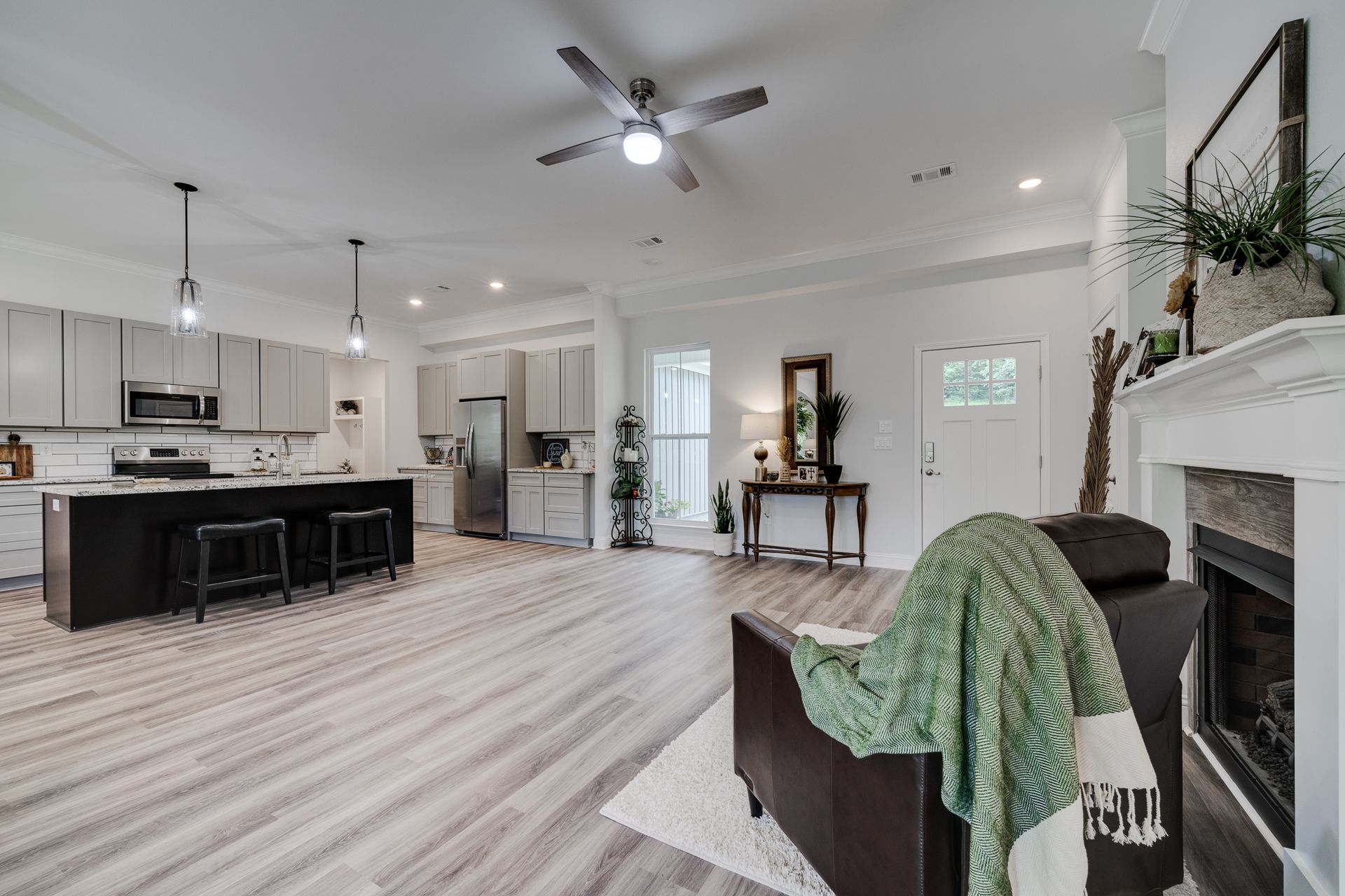 Open-concept kitchen and living room with gray cabinets, black island, and fireplace; light wood floors.